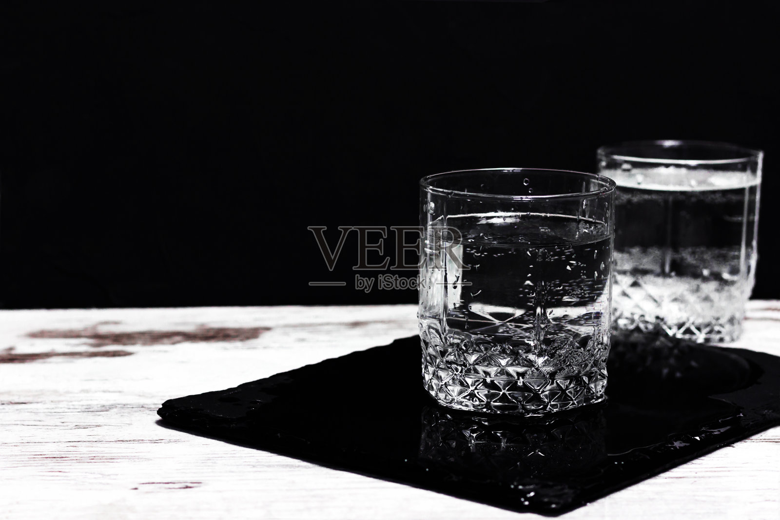 白色桌子上的杯子里有水，背景是黑色。照片摄影图片