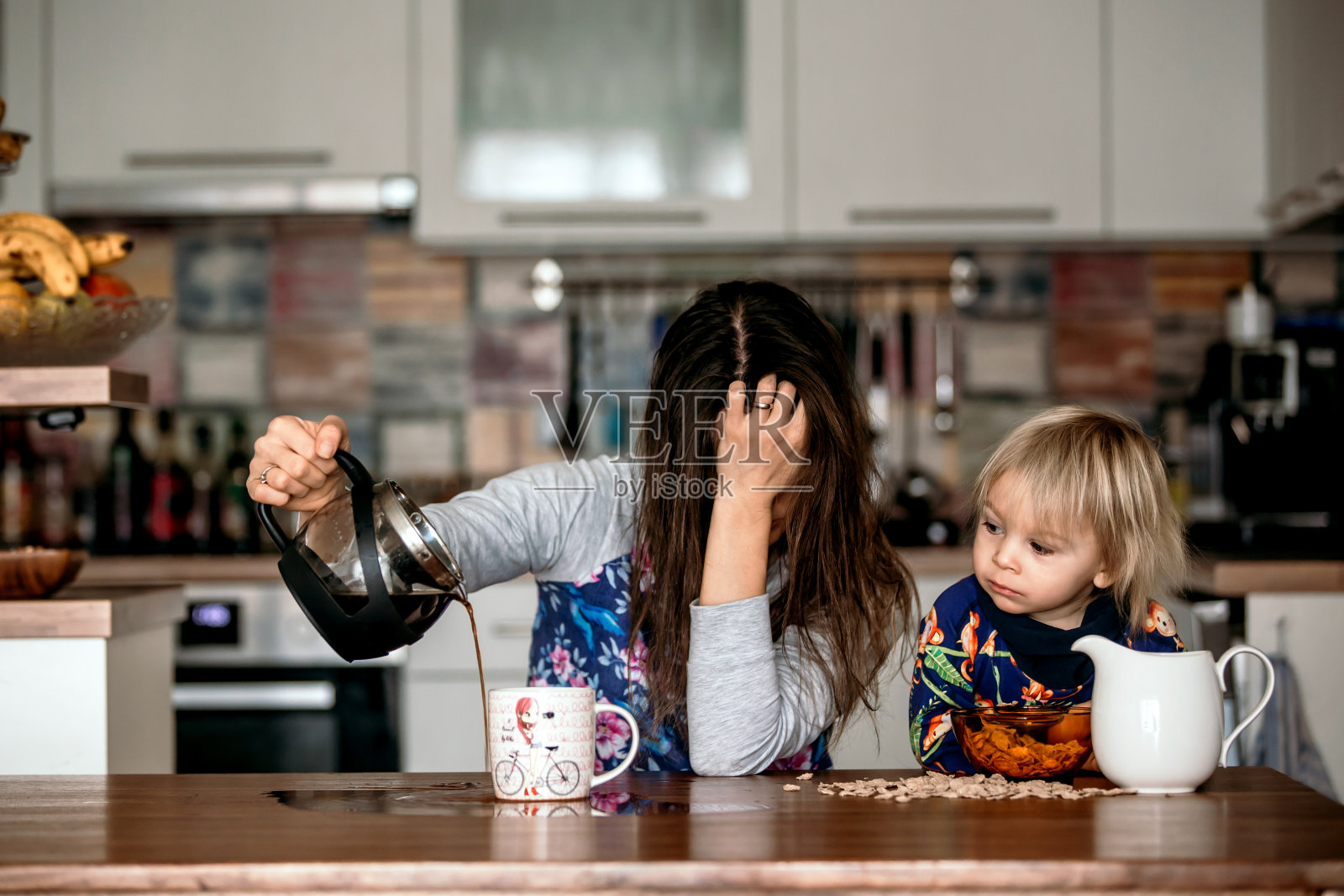 疲惫的母亲，试图在早晨倒咖啡。一夜未眠的女人躺在厨房的桌子上照片摄影图片