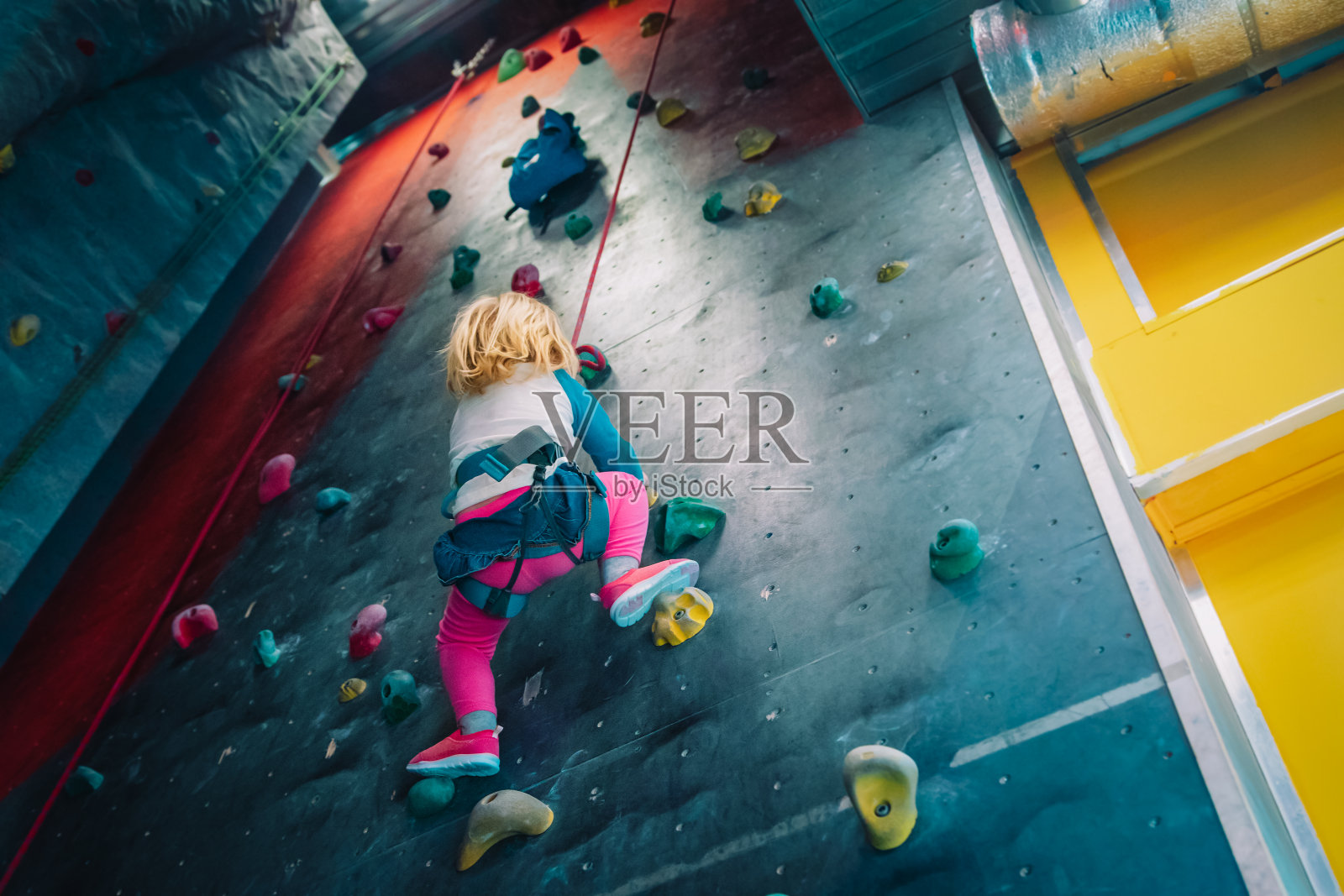 小女孩爬在体育馆的人造巨石墙上照片摄影图片