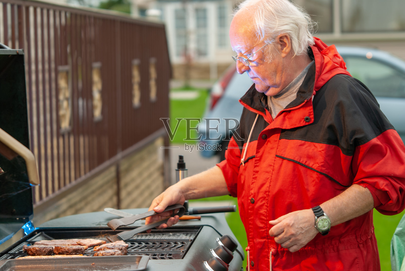 一位穿着红色外套的老人正在烤肉照片摄影图片