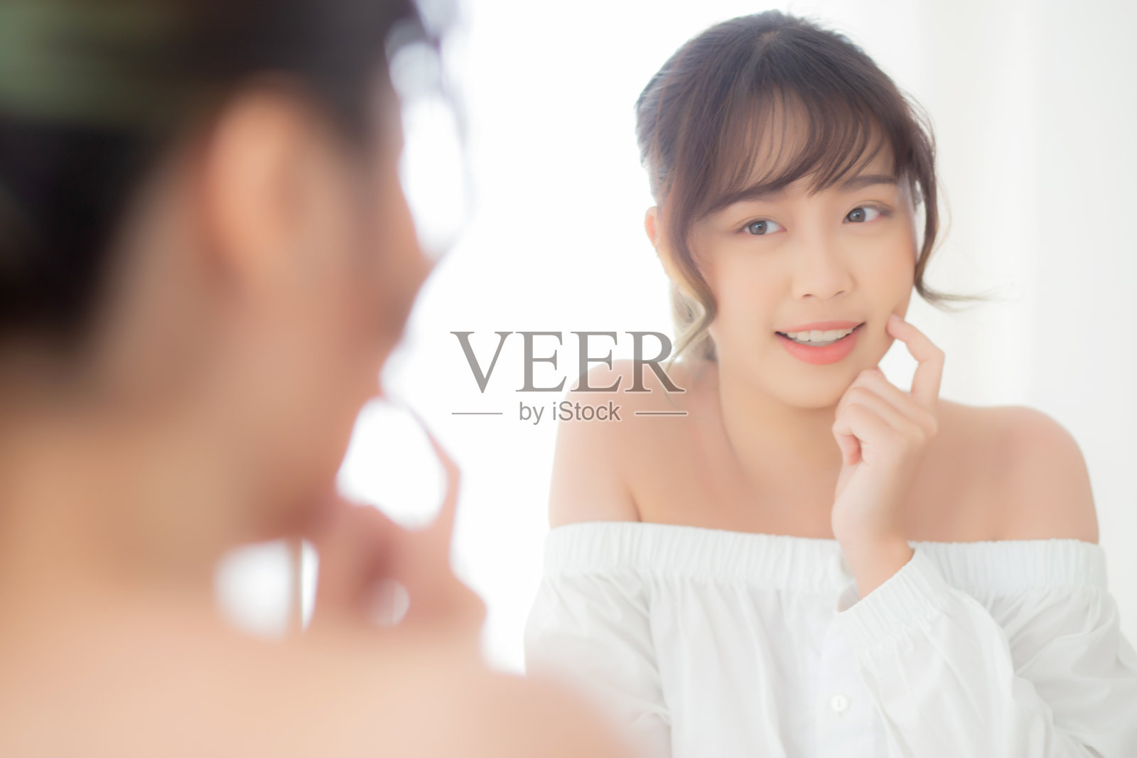 美丽的脸年轻的亚洲女人用快乐的微笑和照镜子，化妆美丽的脸女孩用护肤和美容治疗，刷新女性和清洁迷人，健康的概念。照片摄影图片
