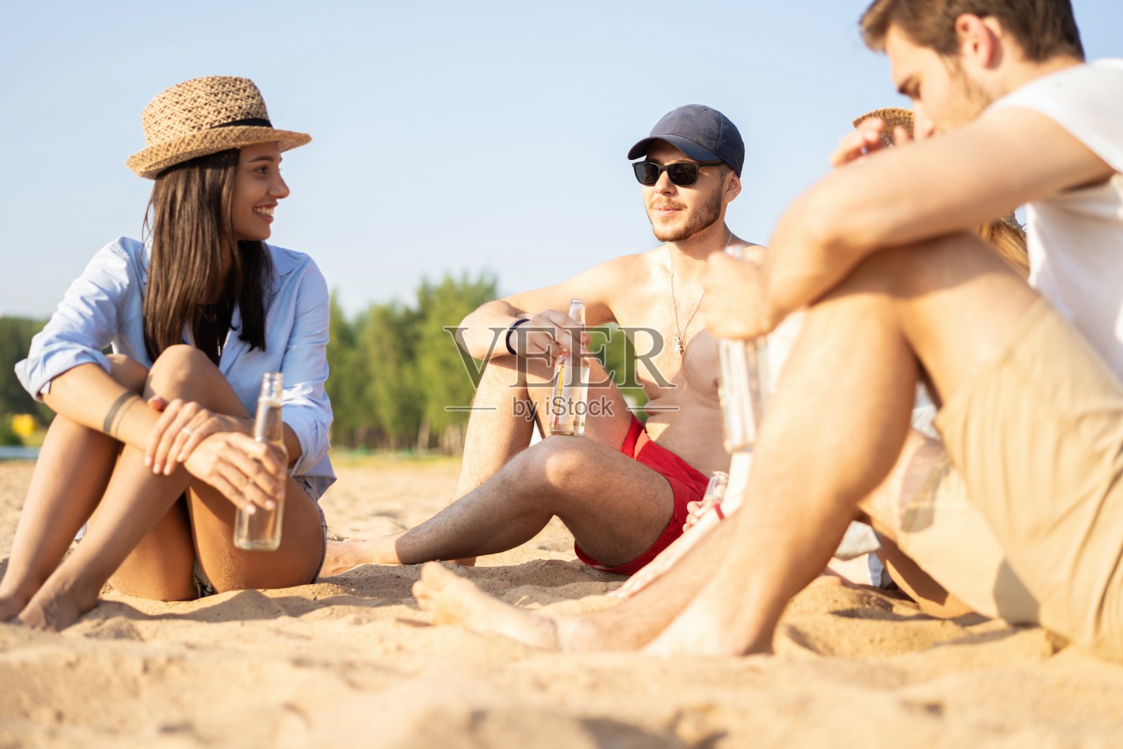 一群快乐的年轻人坐在海滩上聊天，喝啤酒照片摄影图片