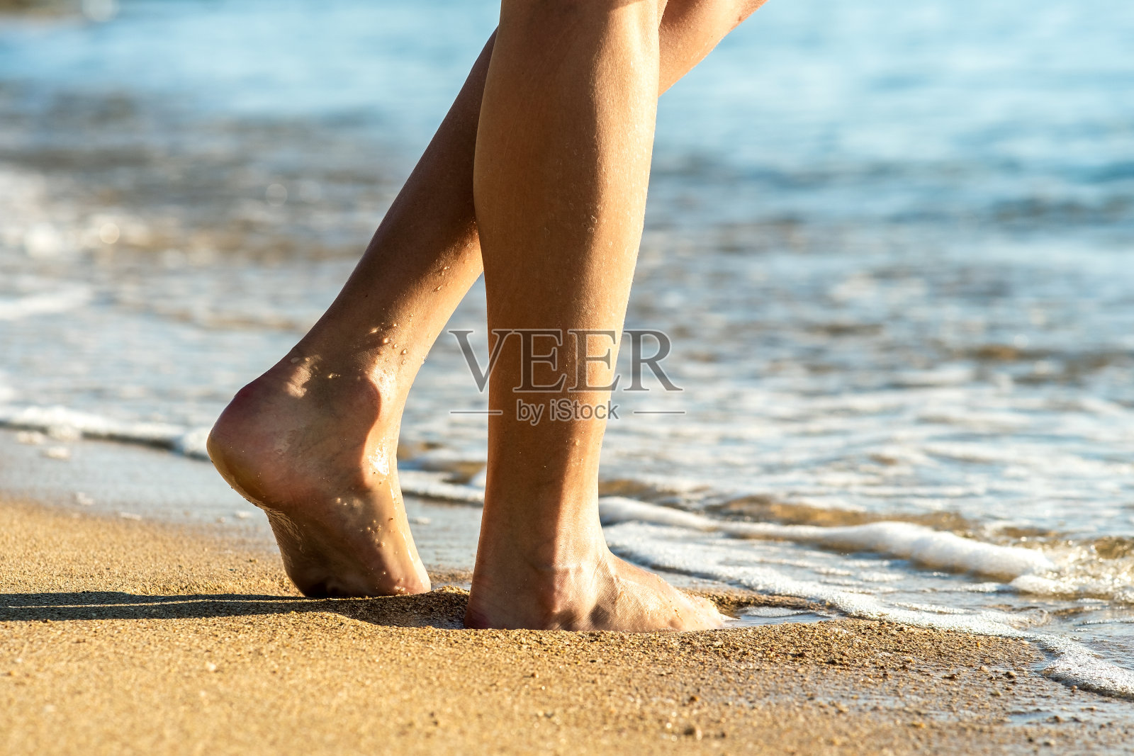 近距离的女人的脚赤脚走在沙滩上留下脚印在金色的海滩。度假、旅行和自由的概念。人们在夏天放松。照片摄影图片
