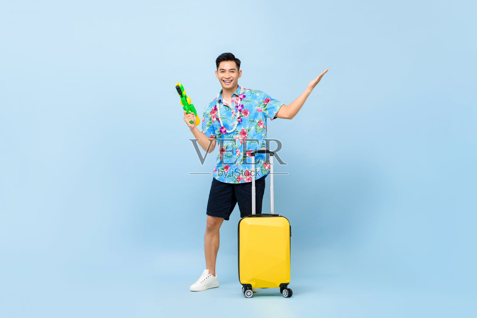 微笑英俊的亚洲游客男子旅行与水枪和行李在宋干节工作室拍摄蓝色背景照片摄影图片