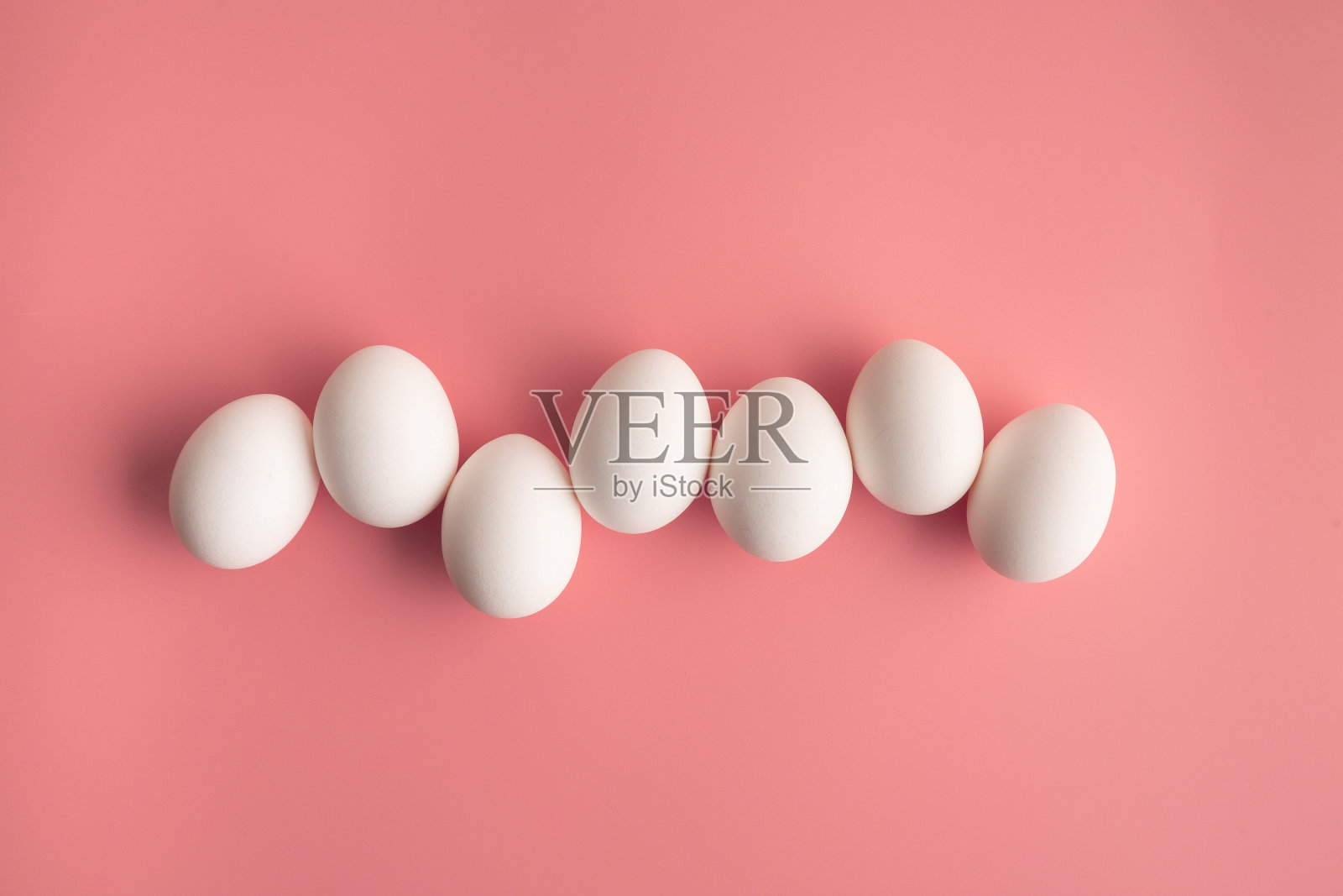 在淡粉色的背景上排列着一排白色的鸡蛋。复活节抽象的概念。照片摄影图片