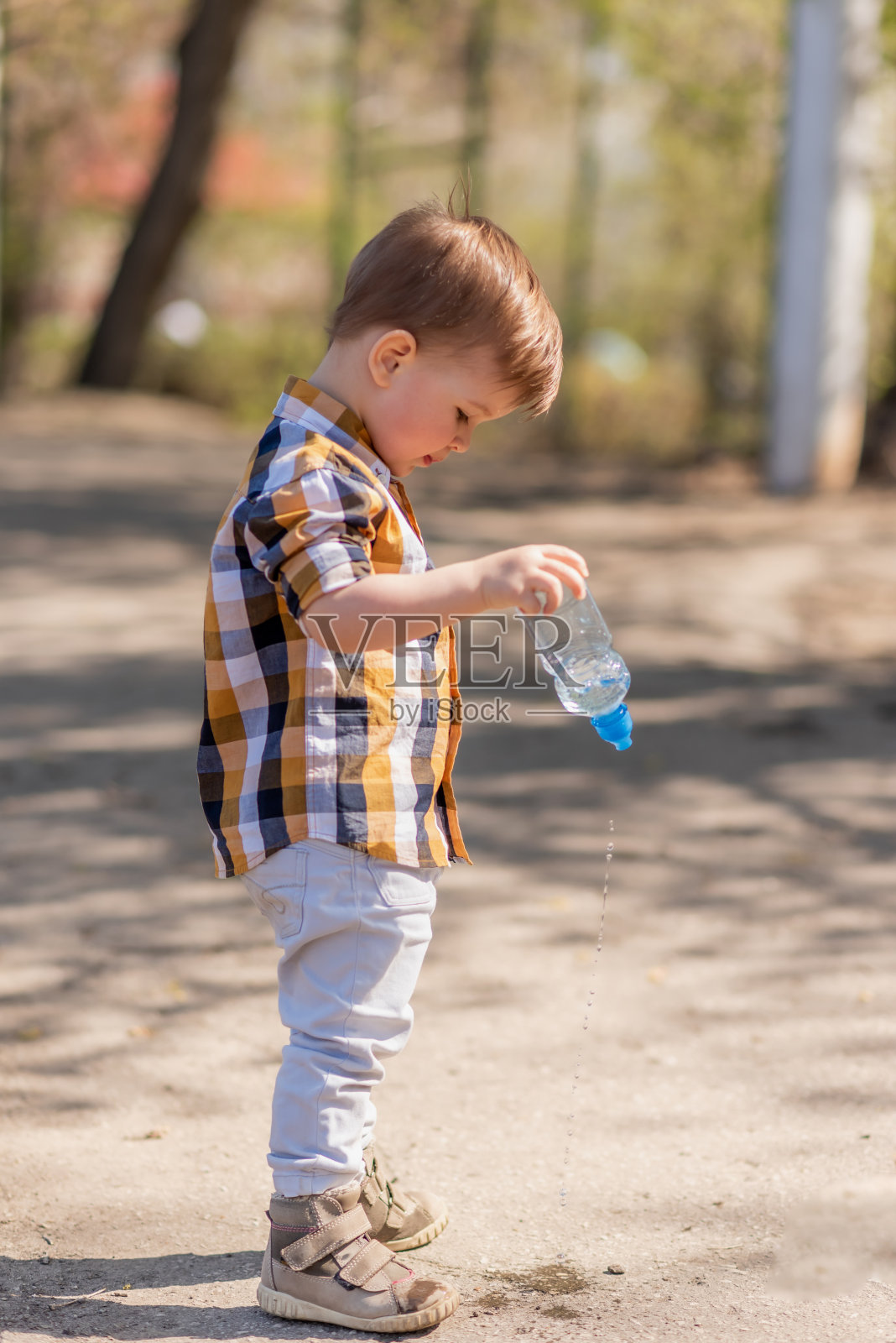 漂亮的孩子把瓶子里的水倒在地上照片摄影图片