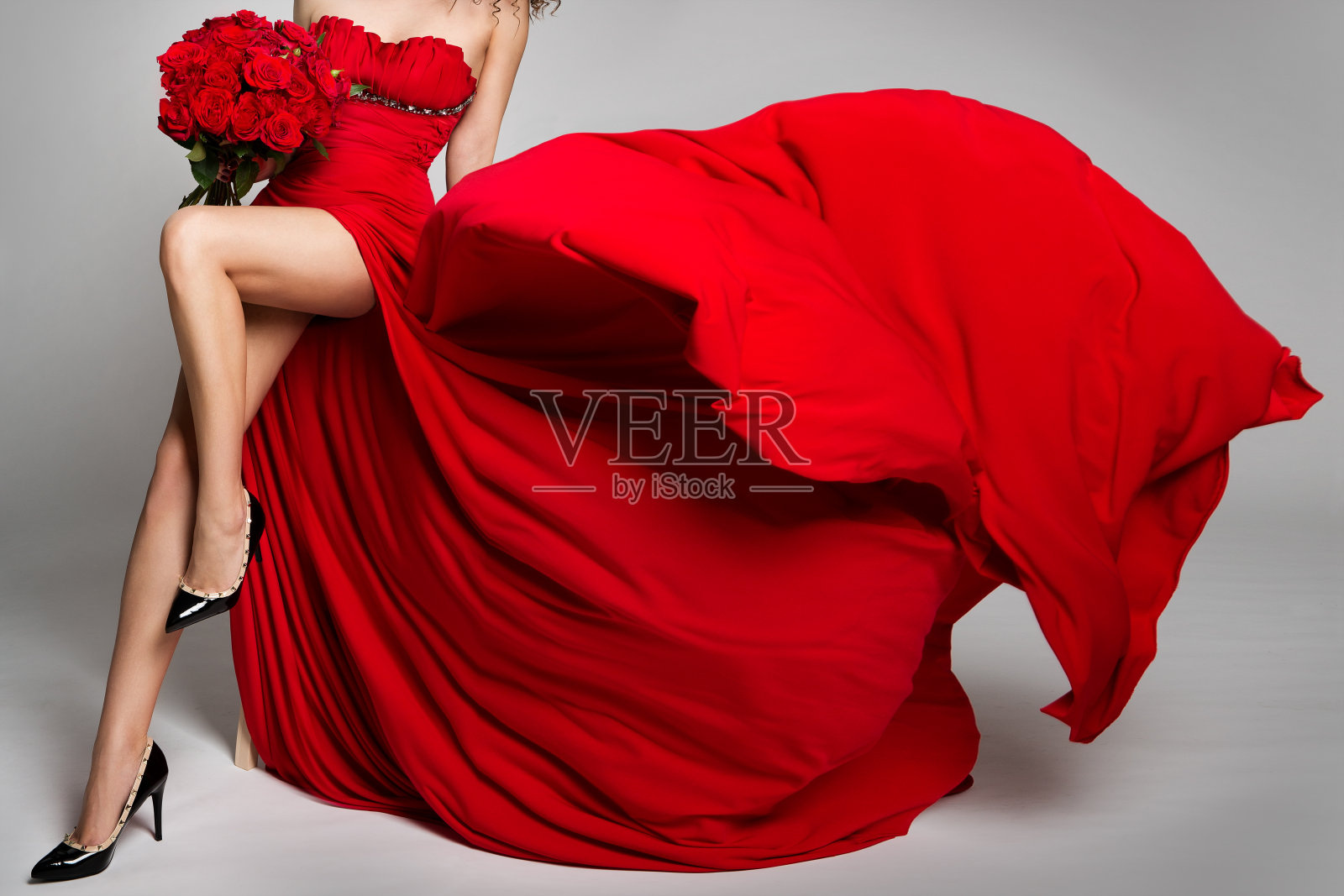 性感女人的腿和花玫瑰，红色连衣裙在风中飞舞，美丽的女孩工作室肖像在飘扬的长袍照片摄影图片
