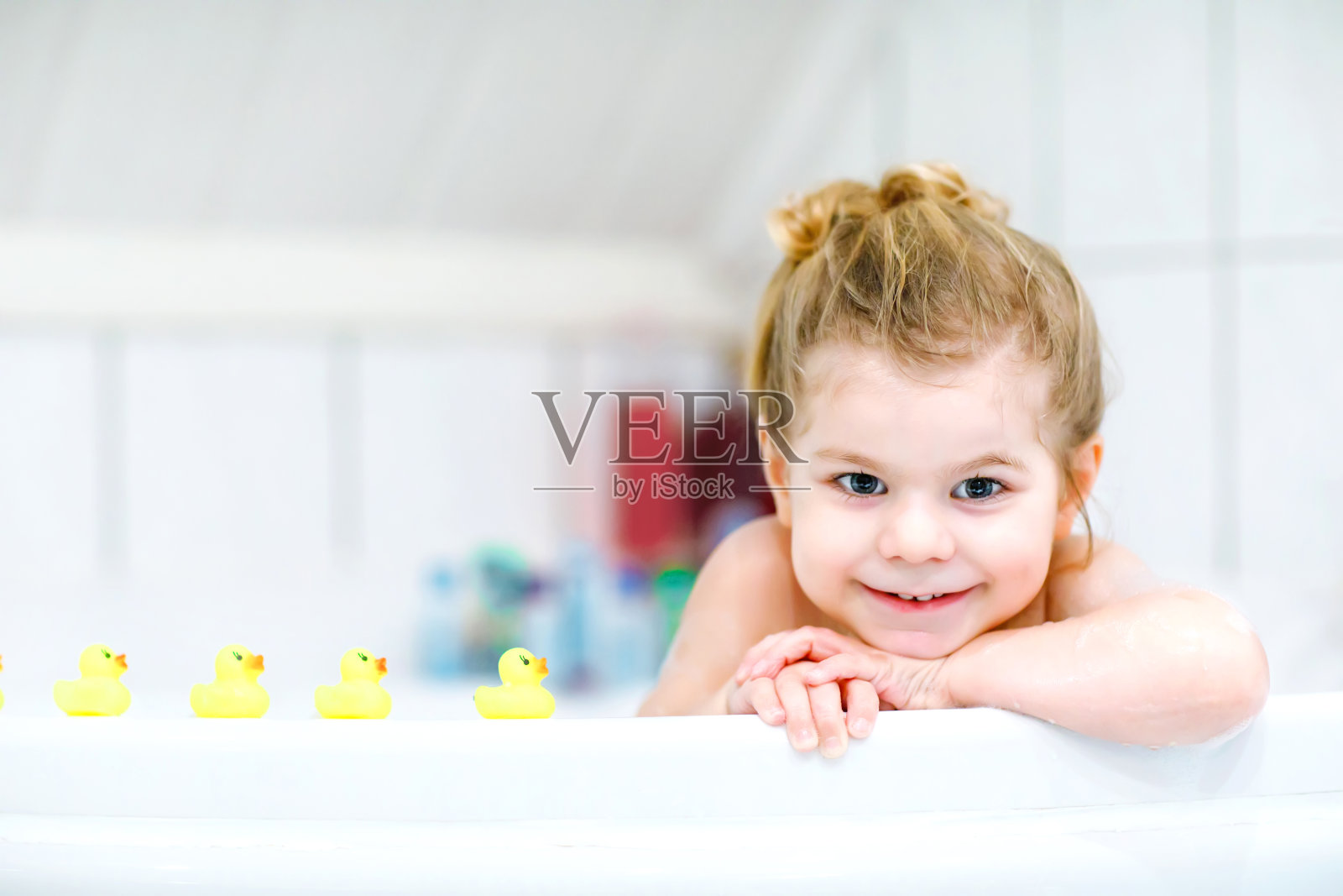 可爱的小女孩在浴缸里洗澡。快乐健康的宝宝玩黄色的橡胶口香糖玩具，玩得开心。清洗，清洁，儿童卫生。照片摄影图片