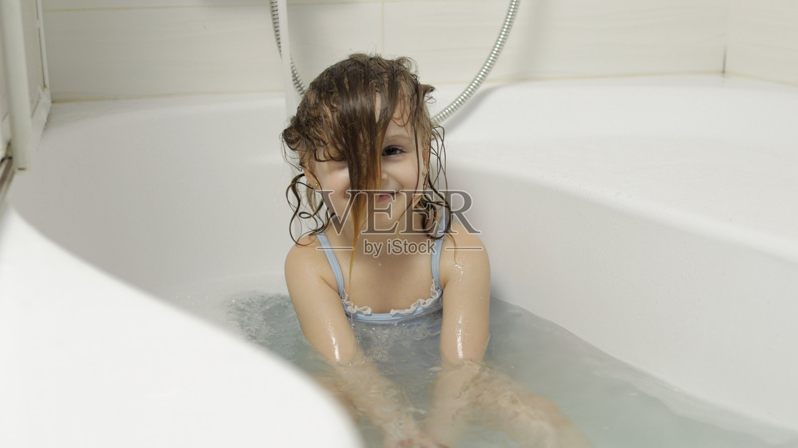 可爱的金发女孩穿着泳衣洗澡。小孩洗她的头照片摄影图片