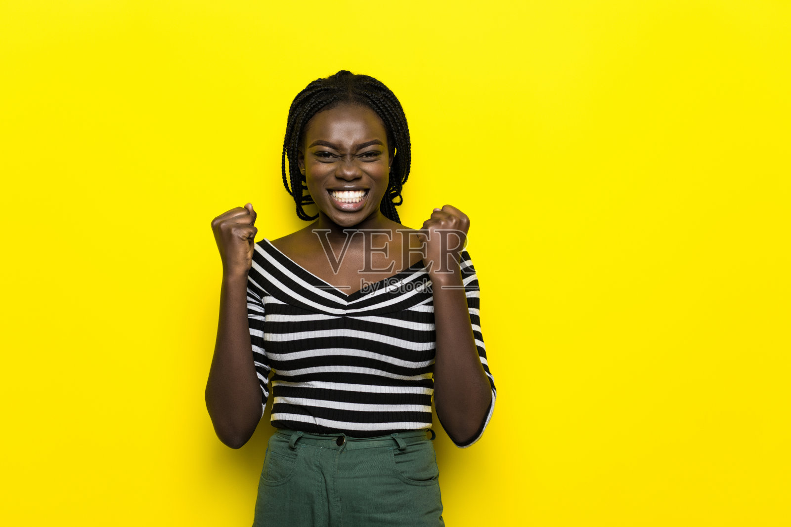 情绪激动的非洲裔美国妇女微笑，举起握紧的拳头在空中，感到兴奋，黄色的背景照片摄影图片