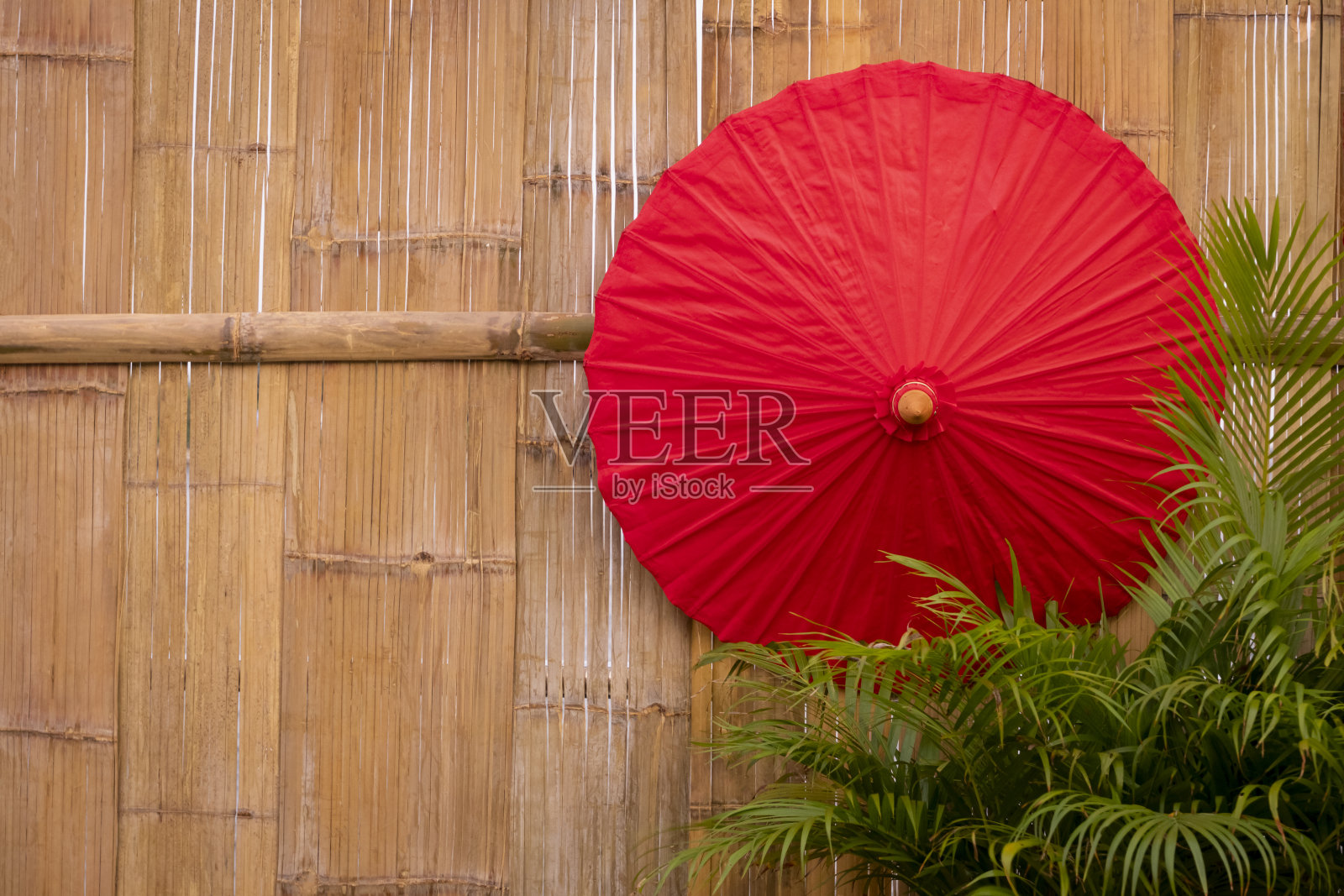 红色的纸伞和绿色的棕榈叶在竹木墙的背景照片摄影图片