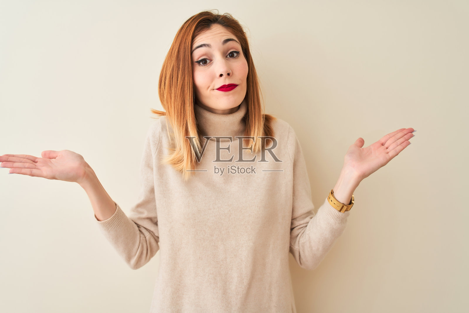 红发女人穿着优雅的高领毛衣站在孤立的白色背景，毫无头绪和困惑的表情与胳膊和手举起。怀疑的概念。照片摄影图片