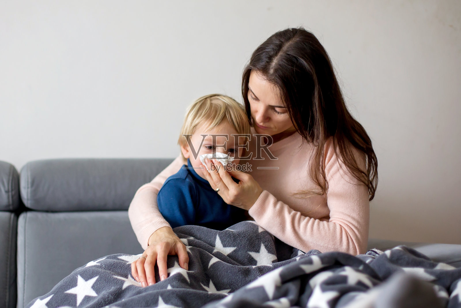 母亲抱着生病的孩子，一起躺在家里的沙发上，发烧流鼻涕照片摄影图片