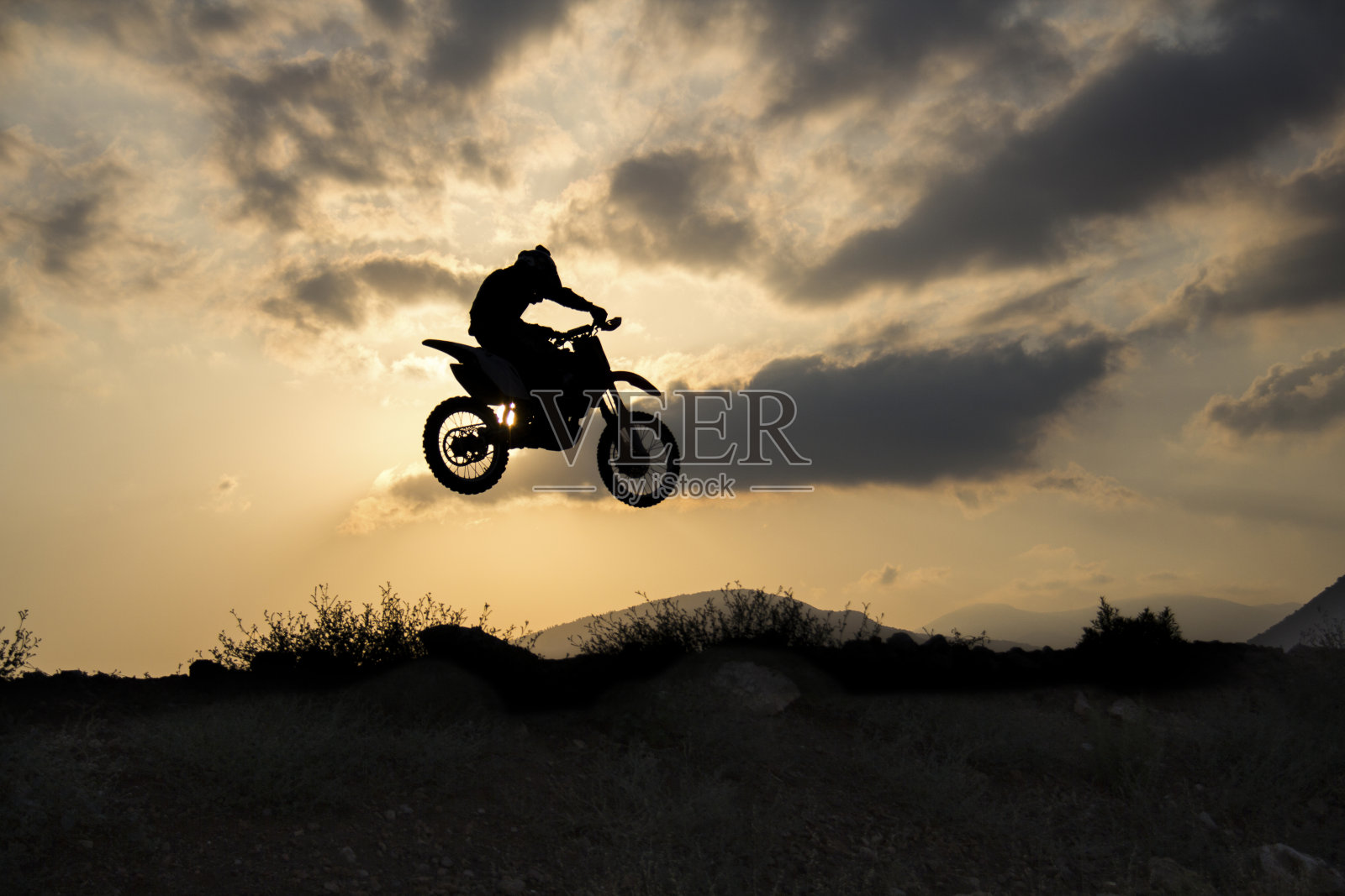 越野摩托车骑手在日落时表演跳高。照片摄影图片