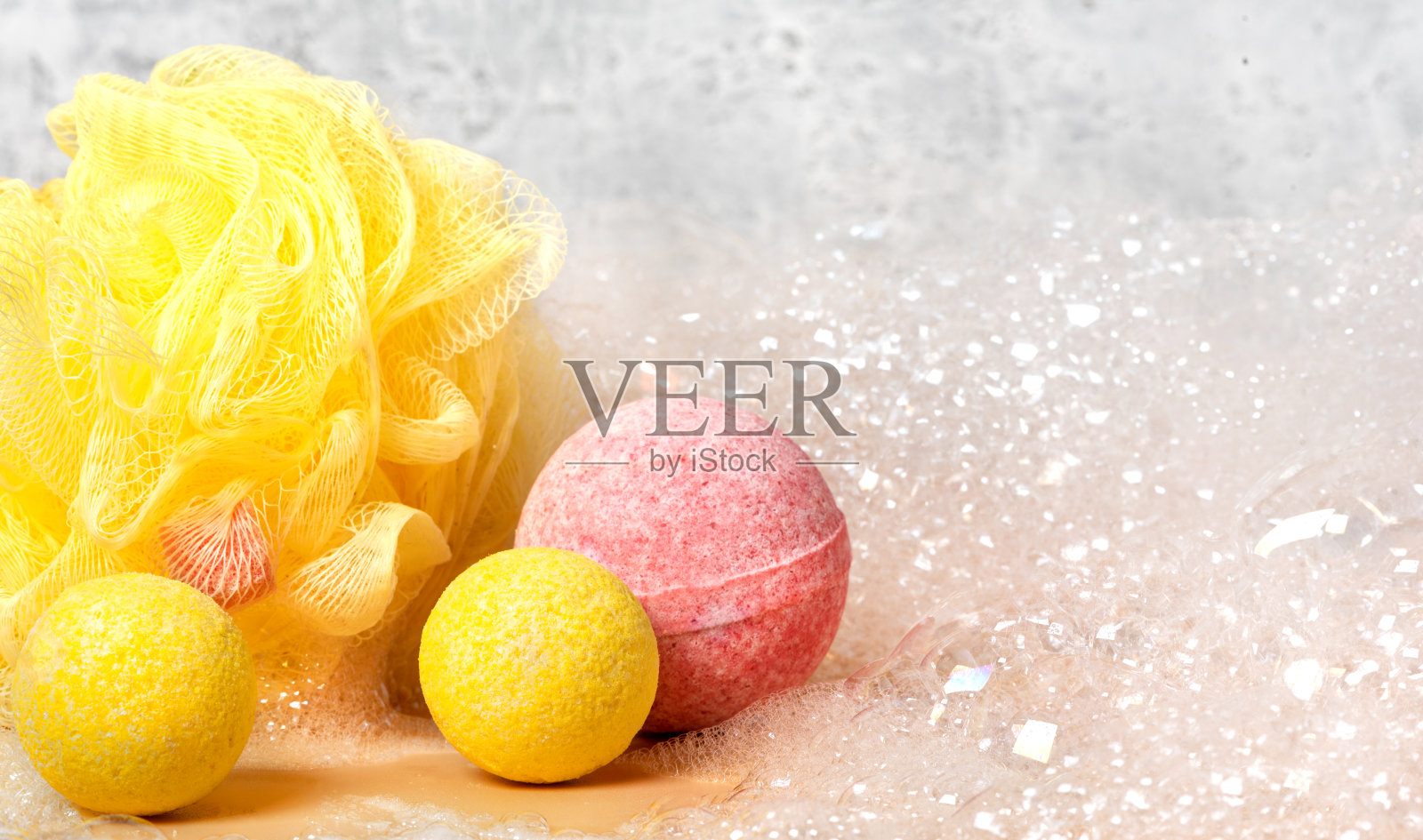 黄色和粉红色的沐浴炸弹和黄色的沐浴海绵肥皂泡沫在灰色的背景照片摄影图片