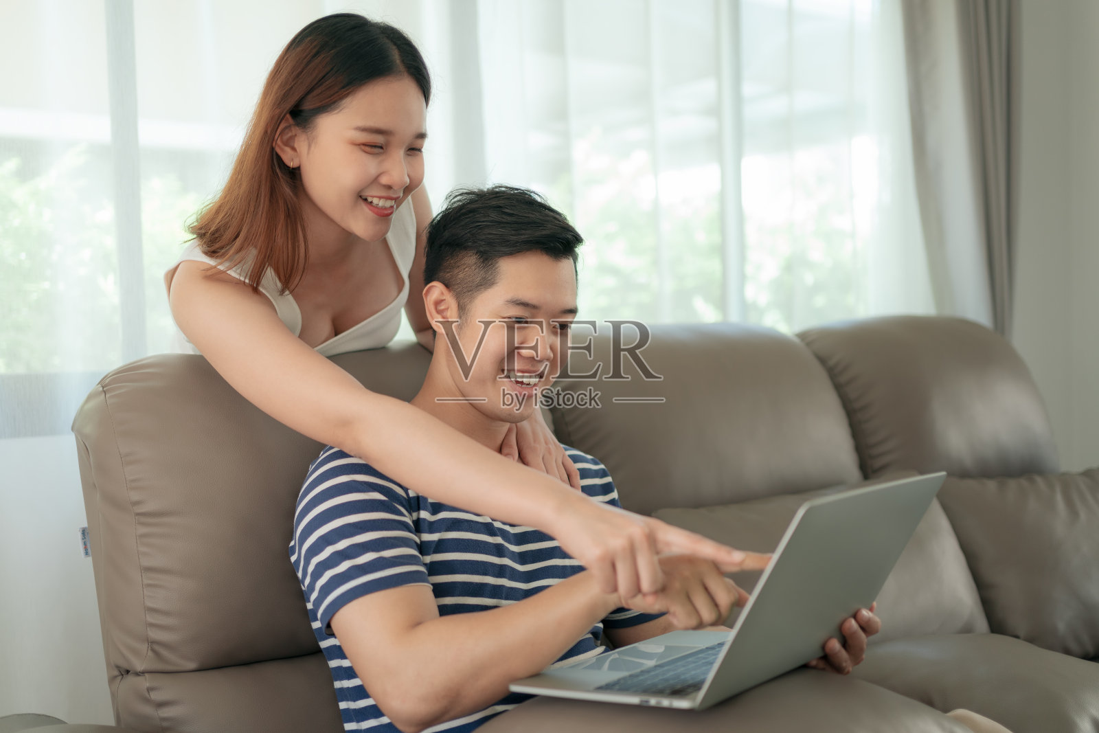快乐的亚洲夫妇用数码平板电脑购物，拿着信用卡，一起坐在家里的沙发上。快乐的生活概念照片摄影图片