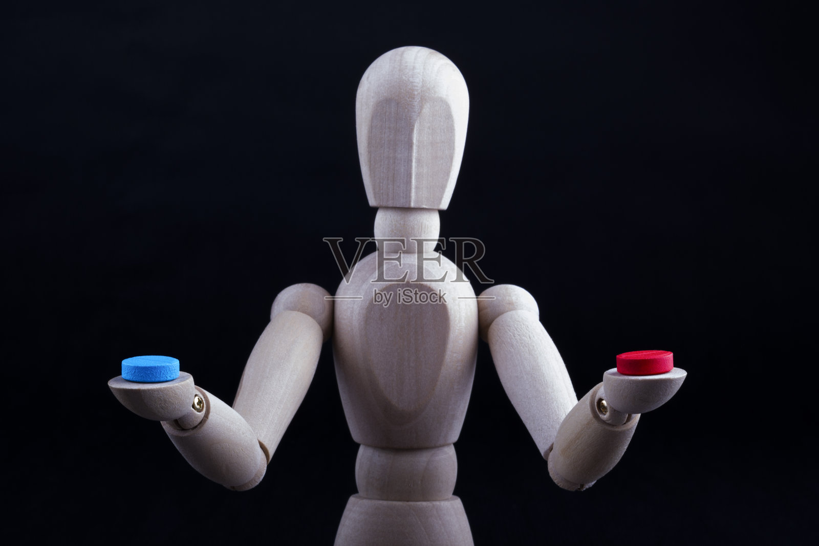 一个木制的完形娃娃或人体模型在黑色的背景上，手里拿着红色和蓝色的药丸。选择的概念。照片摄影图片