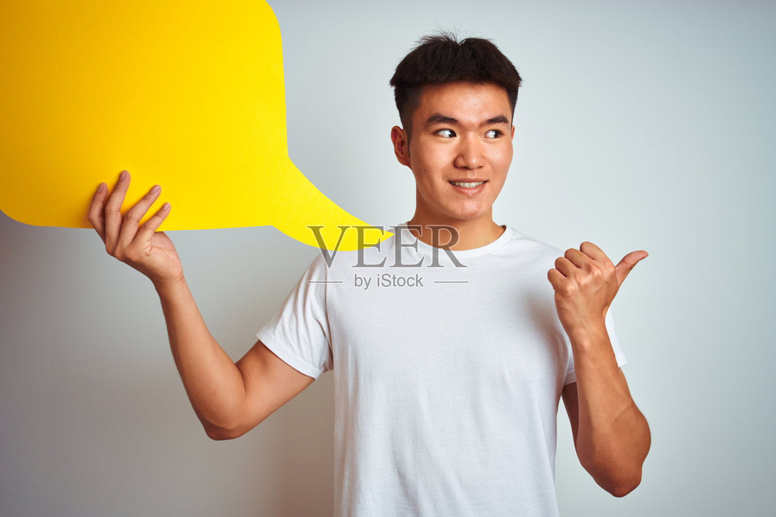 亚洲华人男子持有讲话气泡站在孤立的白色背景指向和显示拇指向上的一边与幸福的脸微笑照片摄影图片