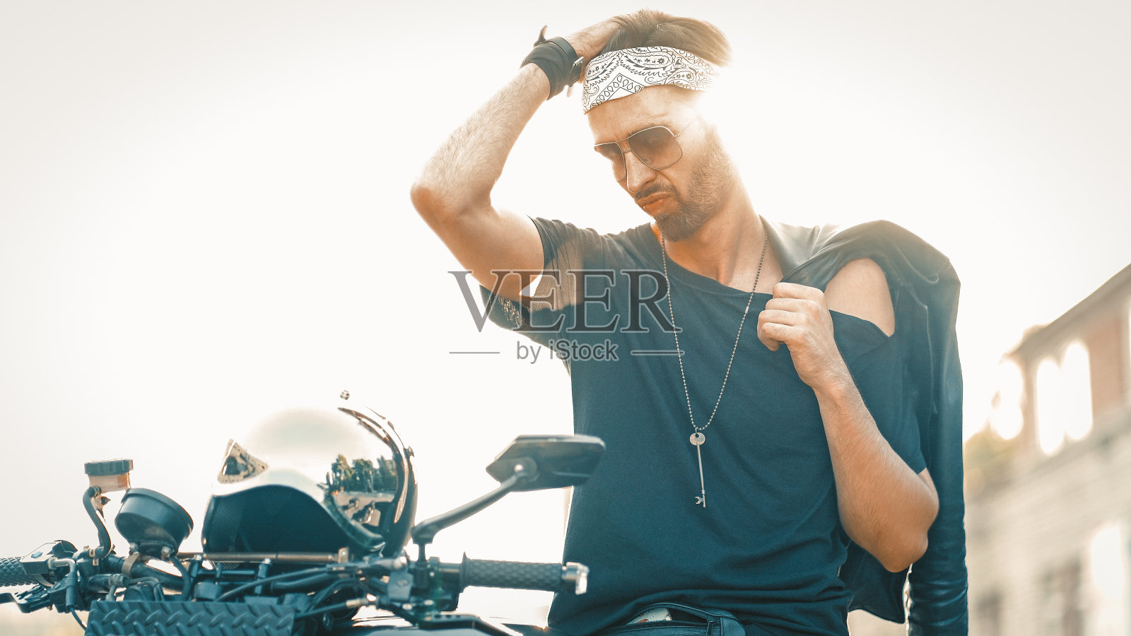 背光下，骑摩托车的人站在摩托车旁边照片摄影图片