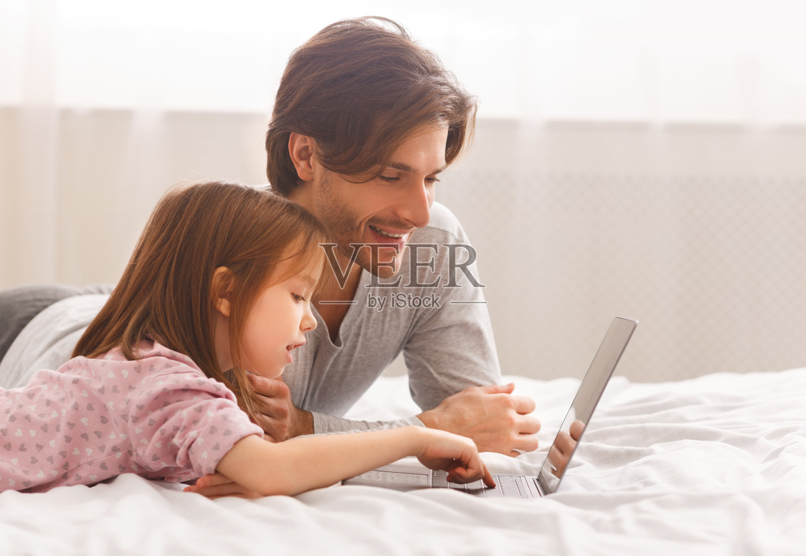 父亲和女儿躺在床上使用笔记本电脑照片摄影图片