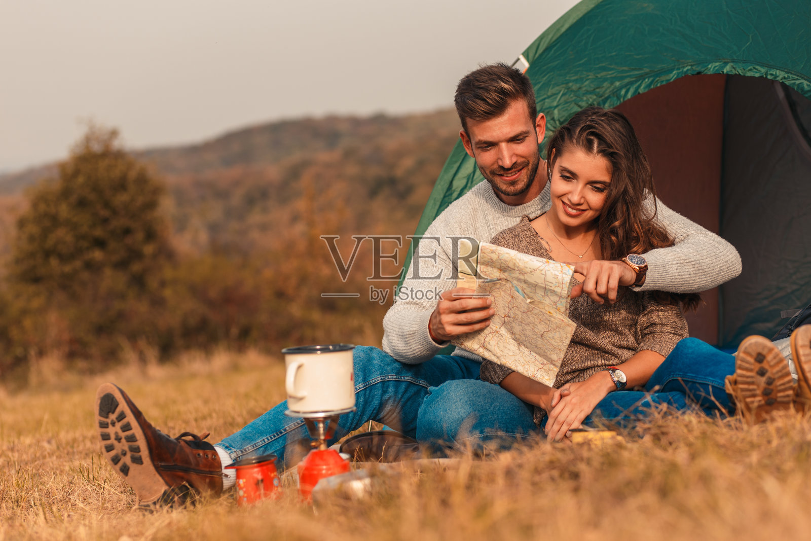 快乐的年轻夫妇坐在帐篷露营花时间在一起。照片摄影图片