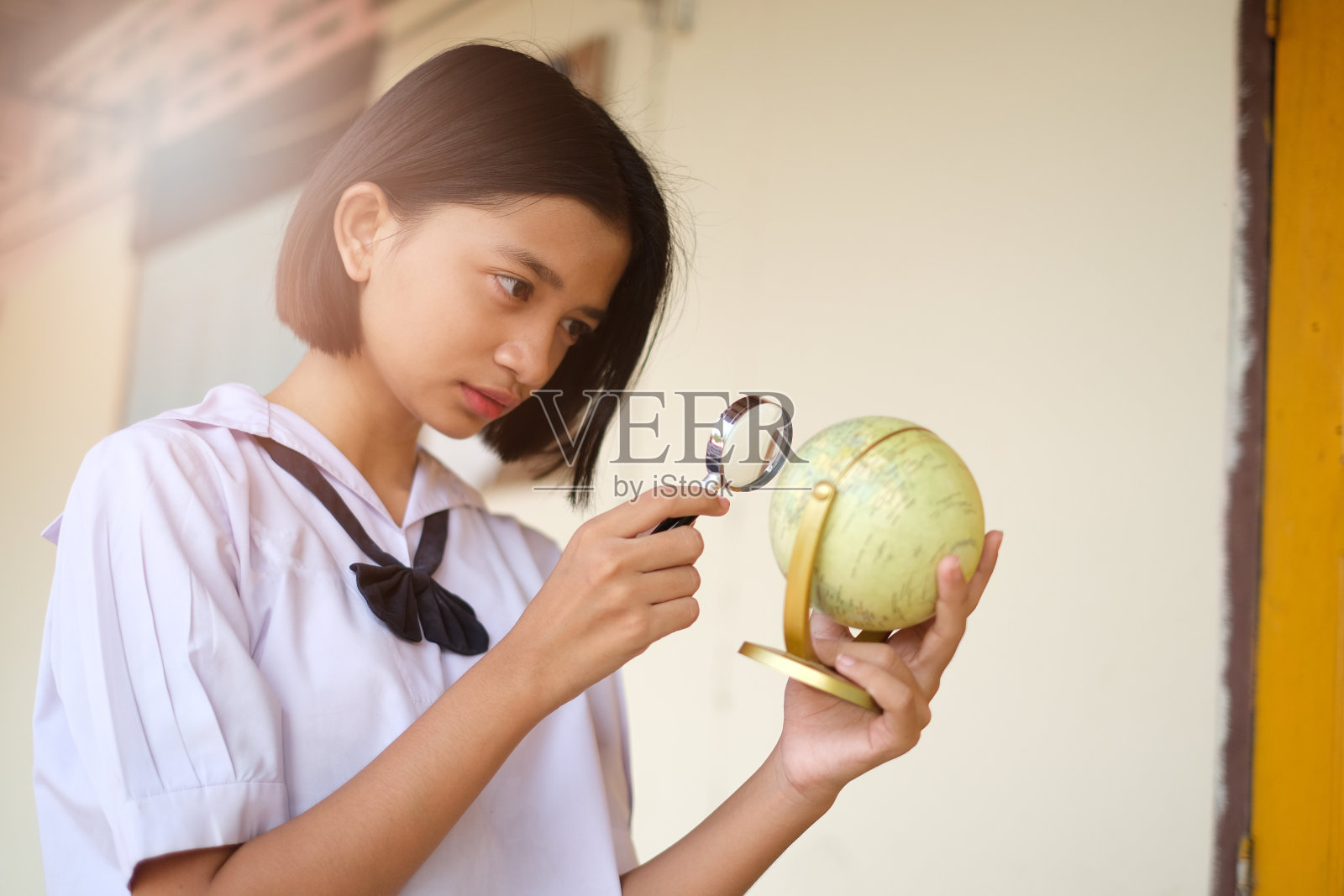 快乐的年轻亚洲女孩与放大镜和地球仪在学校。照片摄影图片