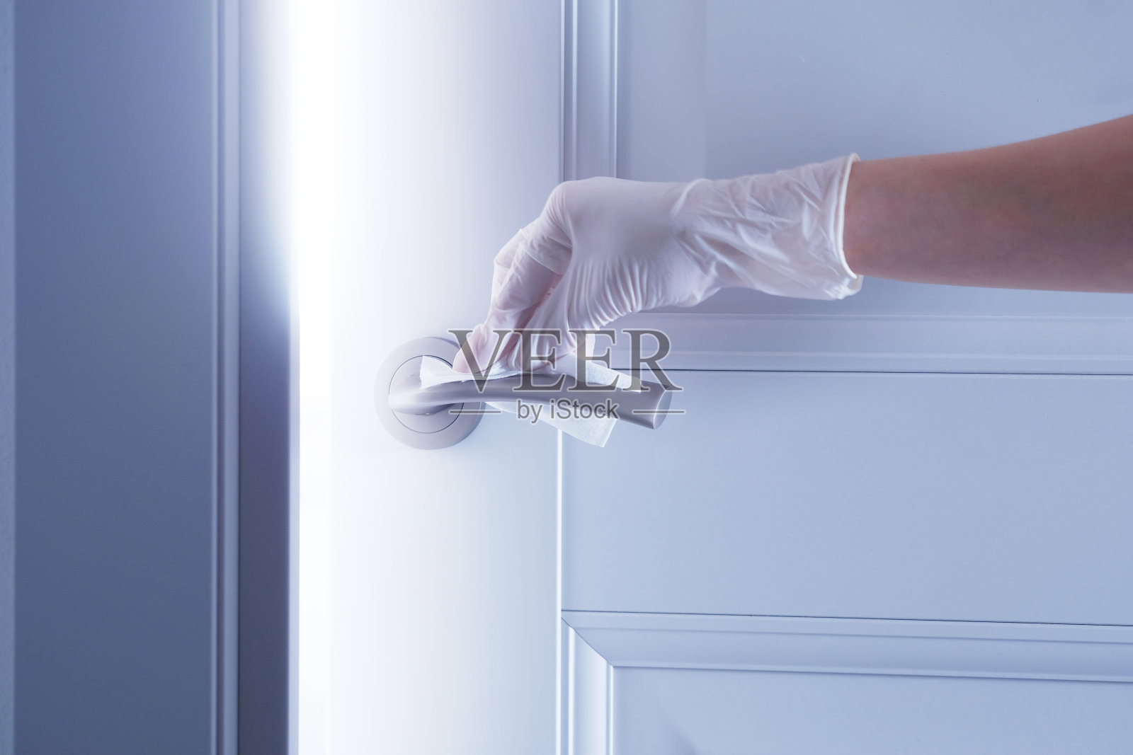 在隔离期间，一位戴着白色医用手套的年轻妇女的手对一扇打开的灰色门的把手进行清洁和消毒，作为一种预防感染和病毒细菌的措施。水平照片与文字的地方照片摄影图片
