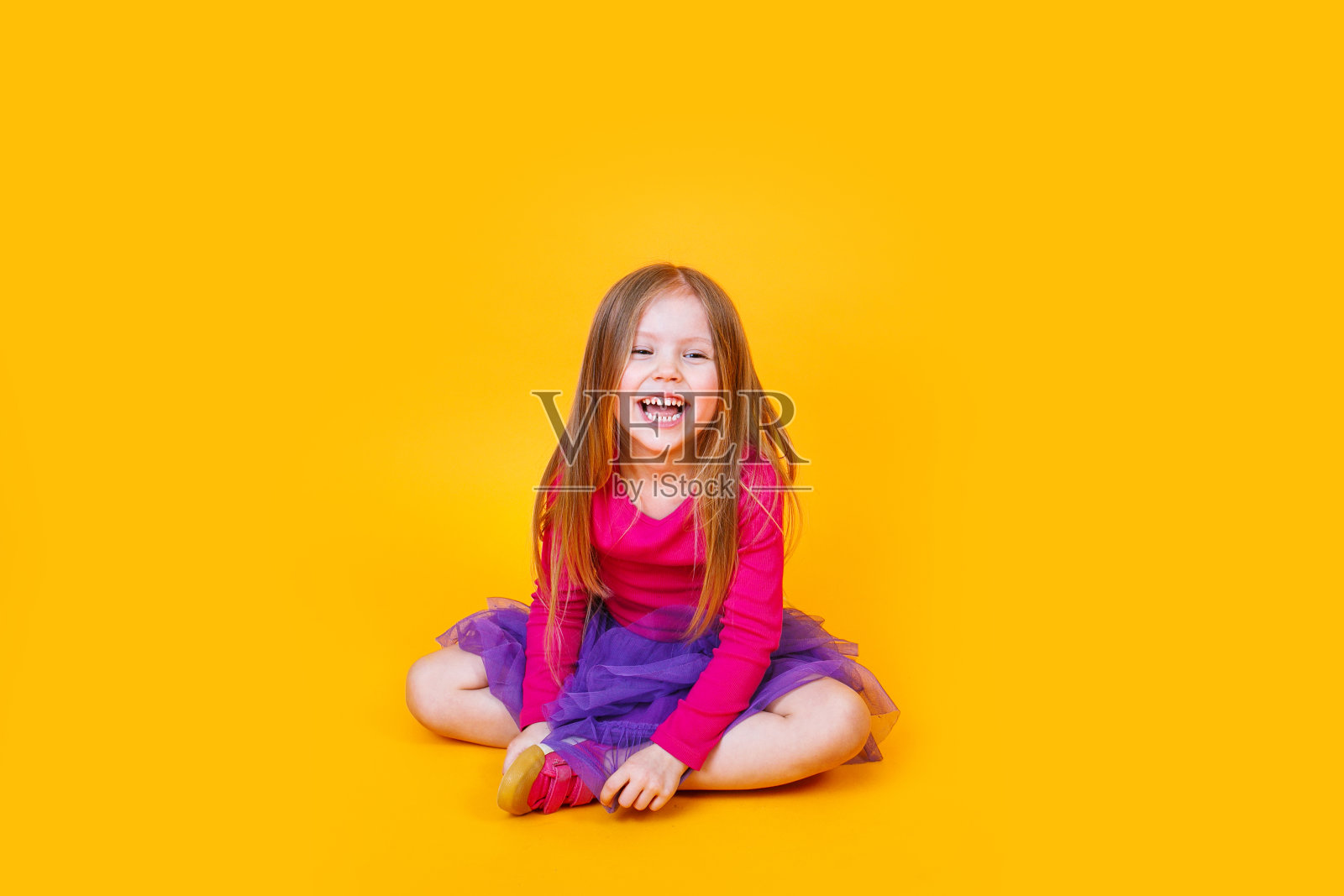滑稽可爱滑稽时尚的小女孩穿着粉红色的t恤和紫色的薄纱裙子坐在黄色的背景照片摄影图片