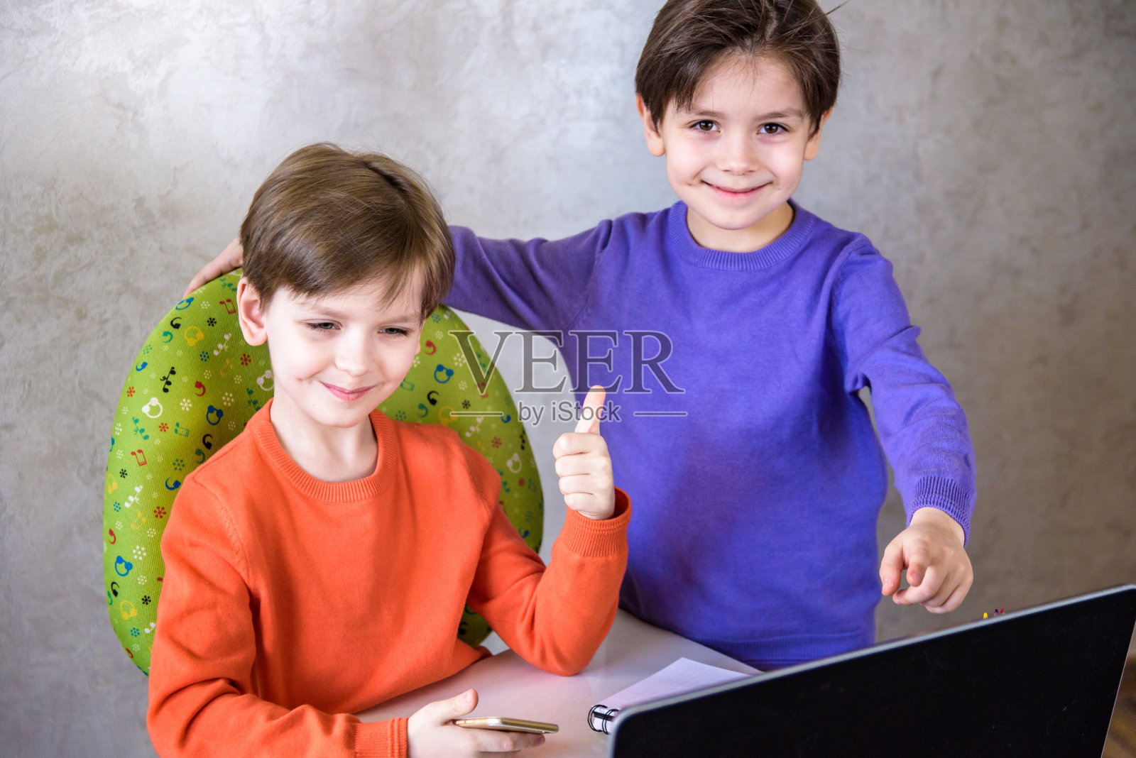 快乐的欣喜若狂的男孩和他的朋友兴奋地尖叫着，在笔记本电脑上玩视频游戏时保持拳头紧握，在他获胜后欢呼，他的小弟弟在后台高兴地微笑。照片摄影图片