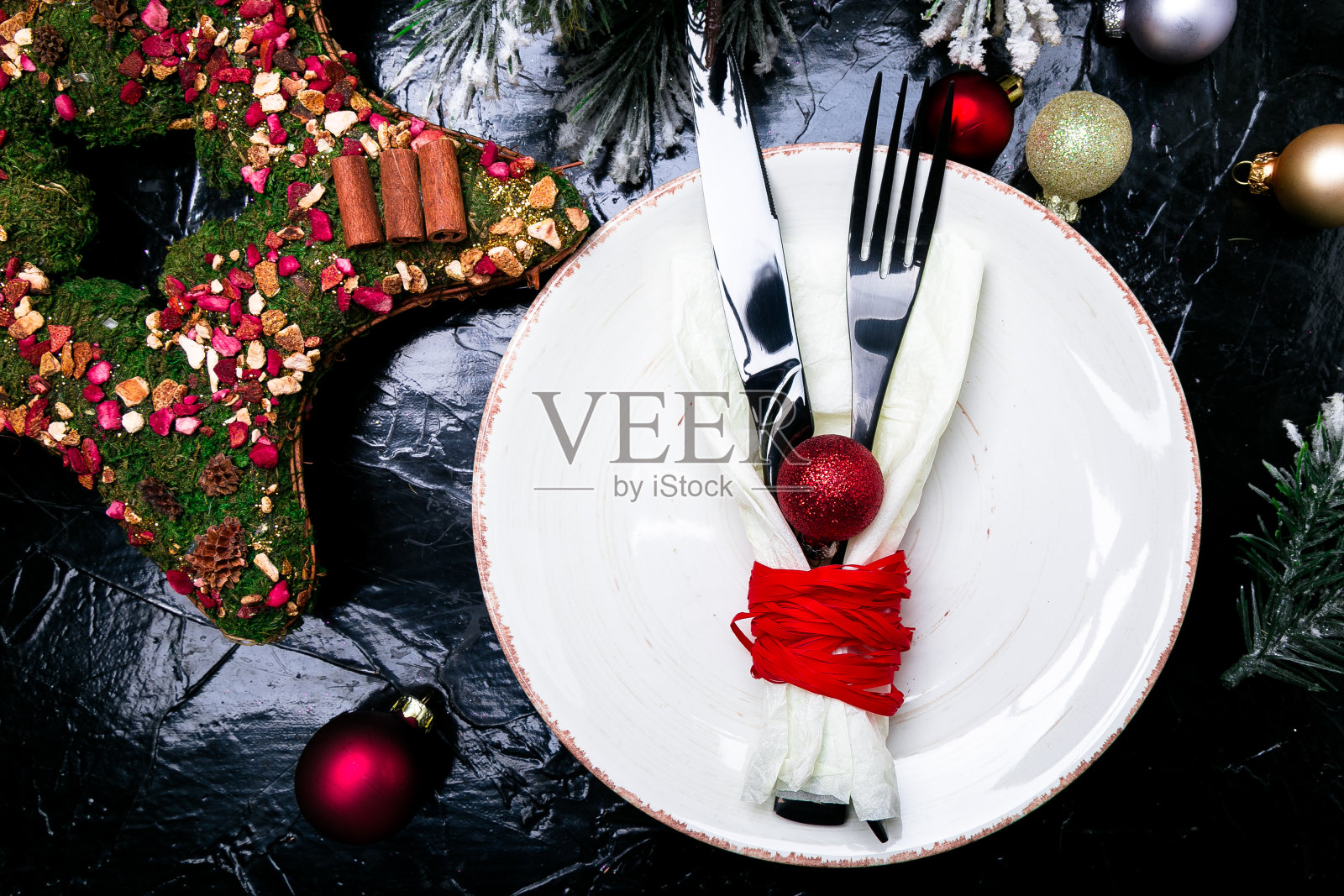 圣诞餐桌摆设。节日的背景。白色的盘子，刀叉与圣诞装饰在黑色的桌子上。前视图。照片摄影图片