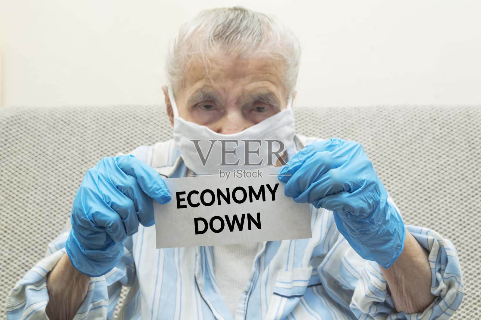 一位老年妇女与保护性医疗口罩在她的脸和保护性手套握纸与文本经济下来照片摄影图片