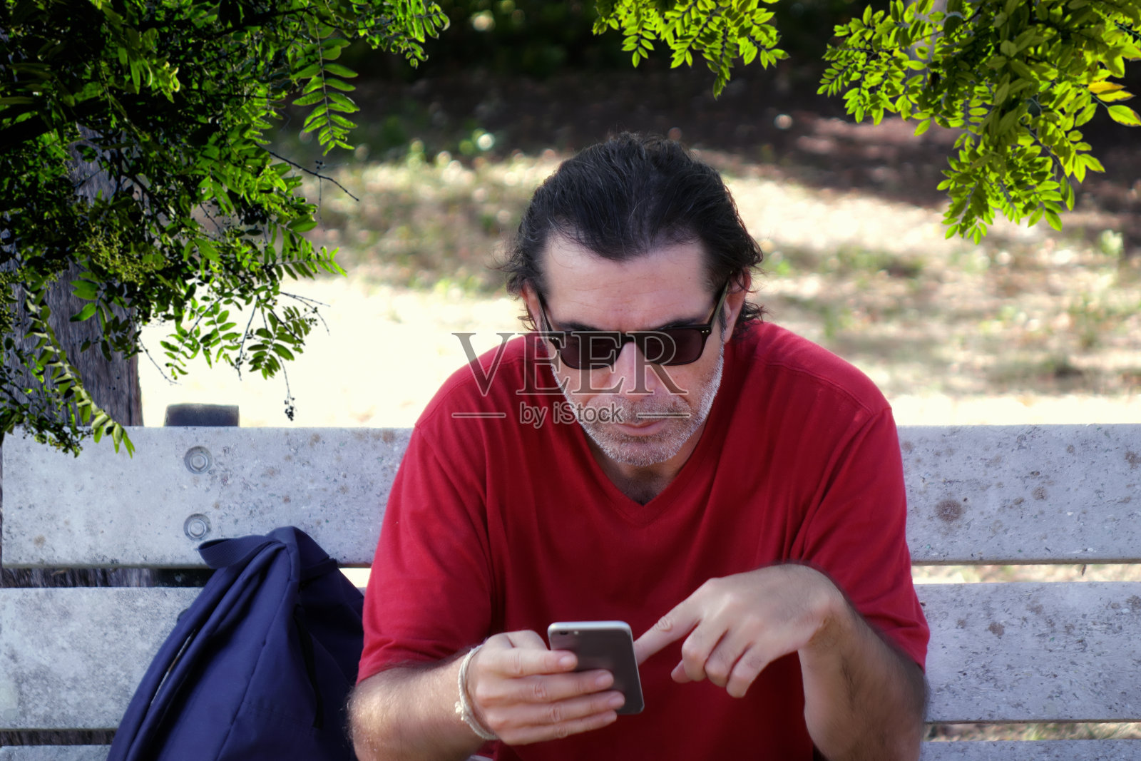 中年男子坐在公园长凳上玩手机照片摄影图片