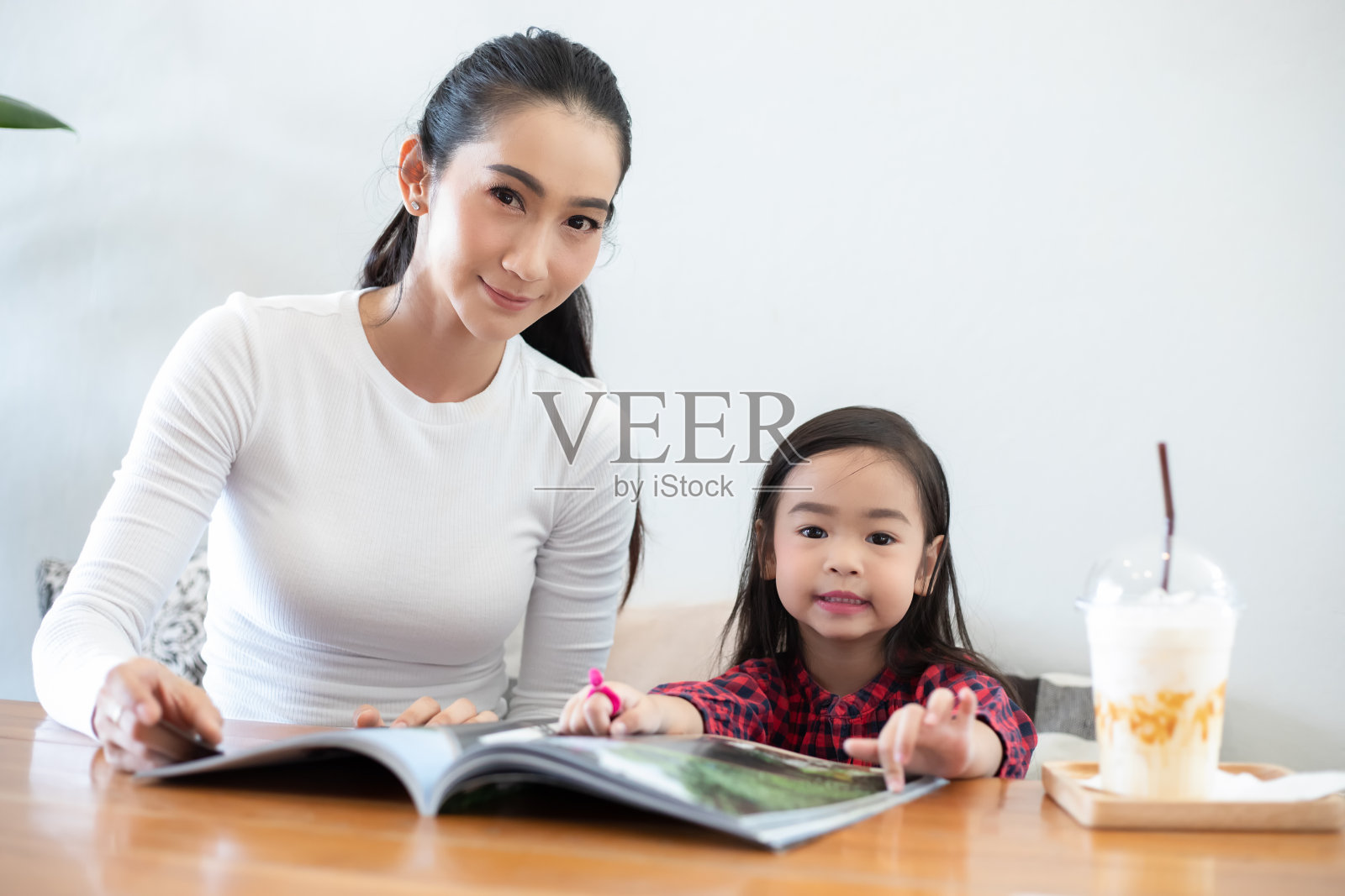 一位亚洲母亲正在教她的女儿在课间休息时在客厅的桌子上看书，家里的桌子上放着冷牛奶。家庭的教育观念和活动照片摄影图片