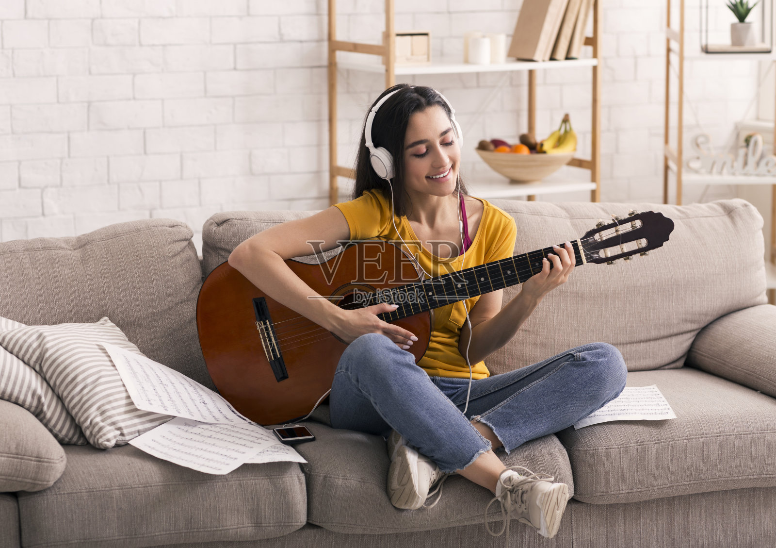 呆在家里进行休闲活动。快乐的女孩戴着耳机在客厅的沙发上弹吉他照片摄影图片