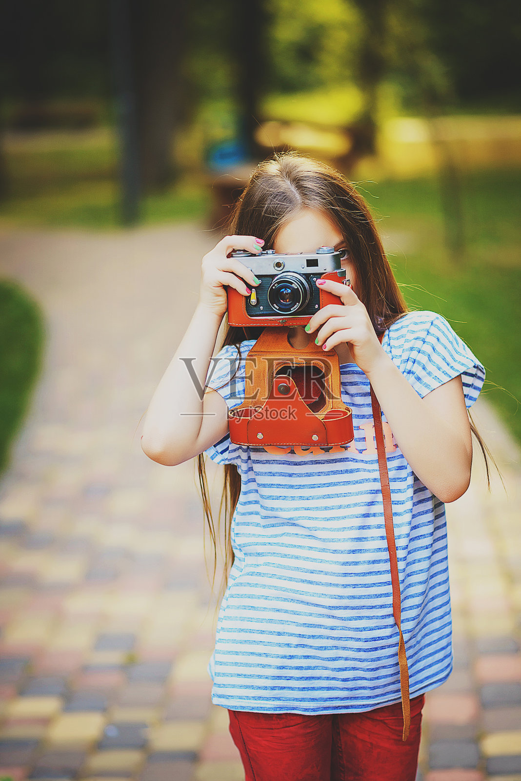 在一片阳光明媚的绿色森林里，美丽的小女孩用老式相机拍下了一张照片照片摄影图片