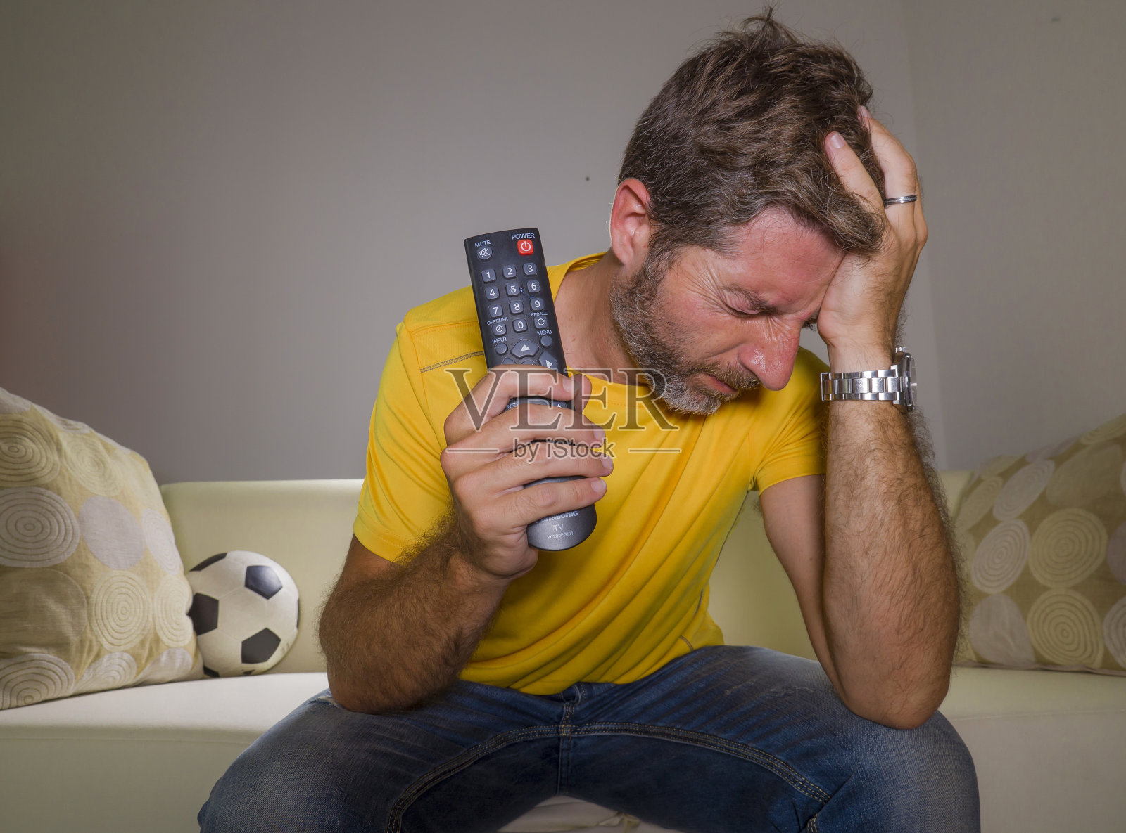 沮丧的球迷在激烈的情绪-家庭肖像年轻沮丧和悲伤的男子看电视足球比赛在客厅的沙发上他的球队输了比赛照片摄影图片
