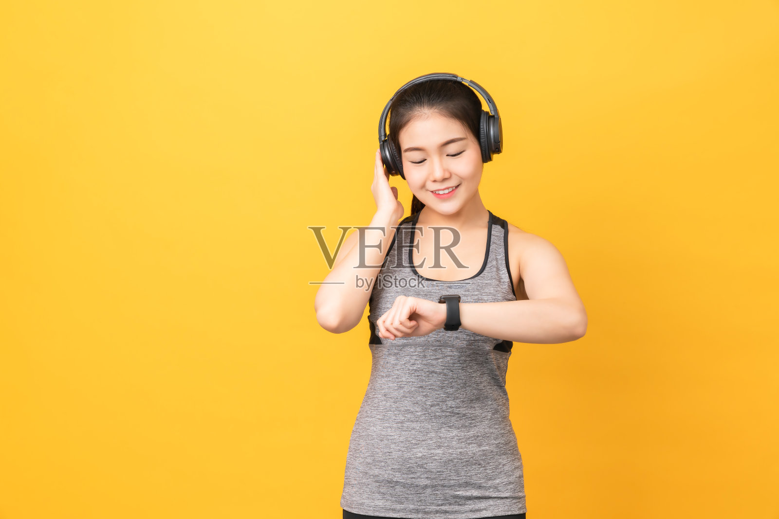 微笑的亚洲女人穿着运动装看起来智能手表和耳机在橙色的背景。照片摄影图片