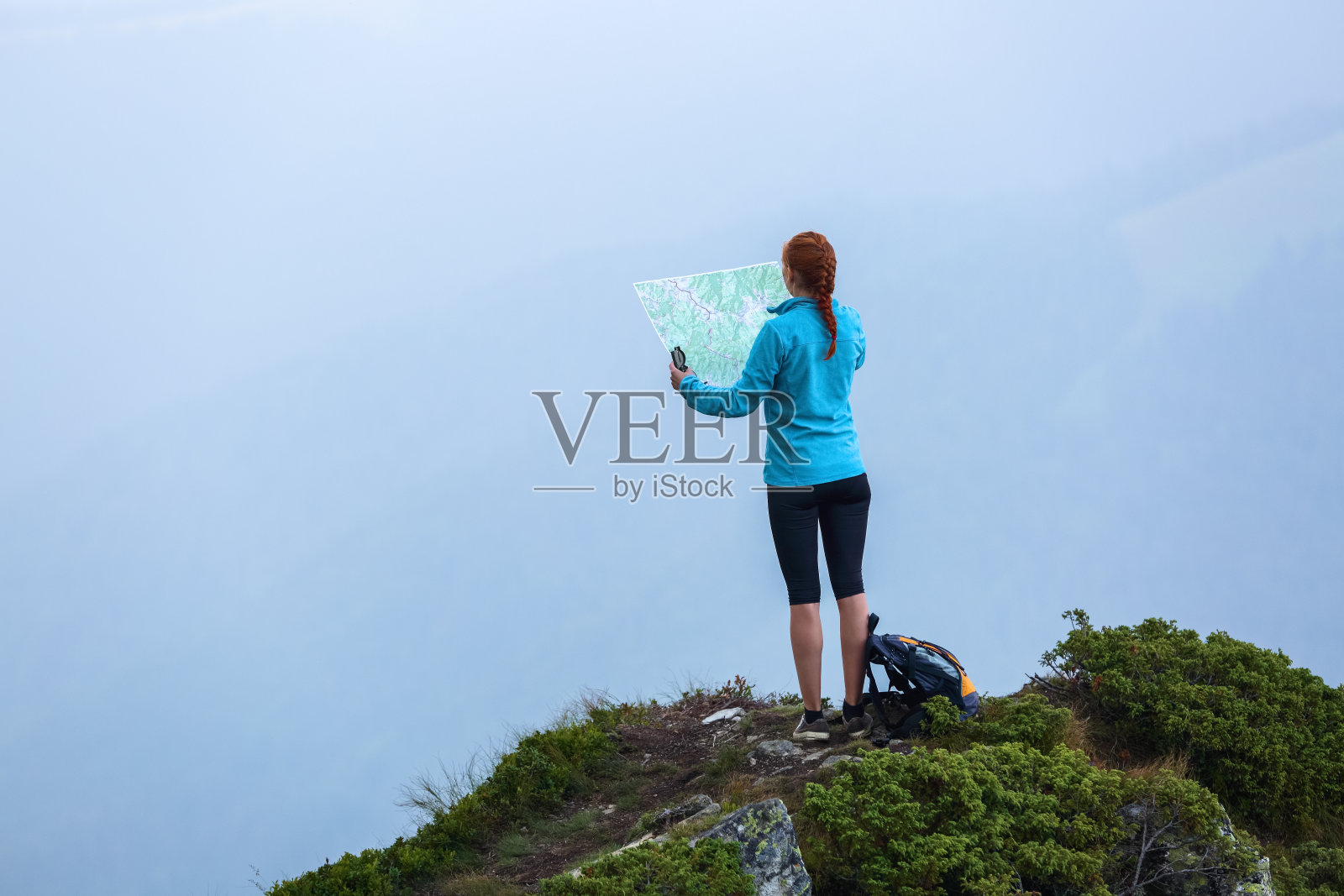 在山顶上，带着地图和指南针的旅游女孩正在寻找梦想的道路。雾中的地平线。夏天的风景。极限运动。照片摄影图片