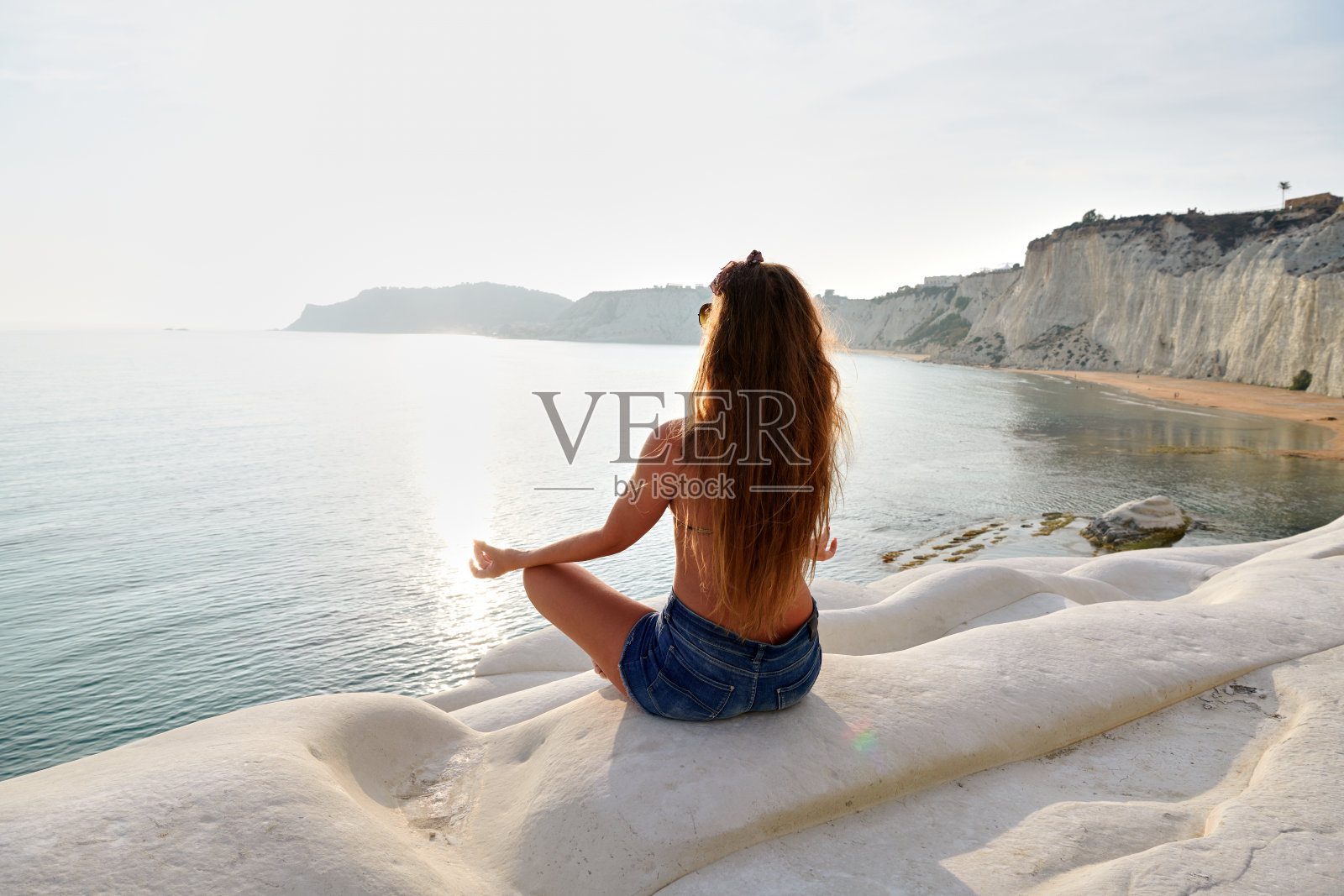 年轻女子在岩石上欣赏日落时的海景照片摄影图片