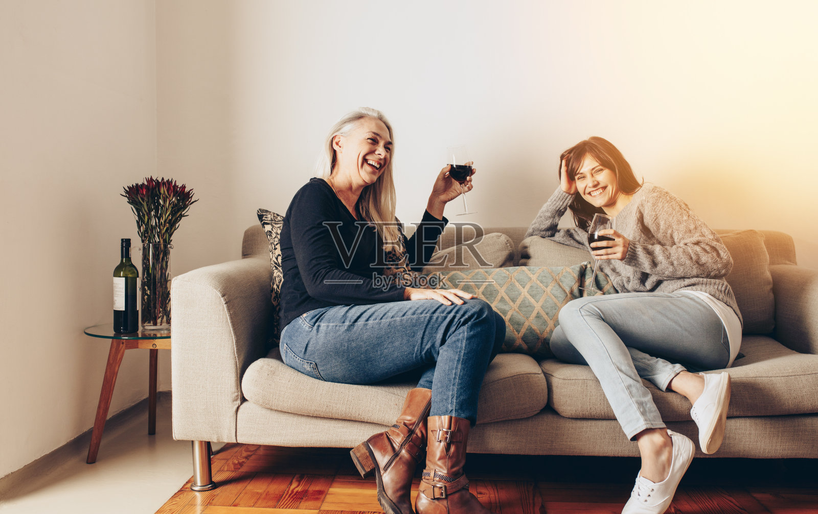 微笑的母亲和女儿在沙发上休息，喝着葡萄酒照片摄影图片