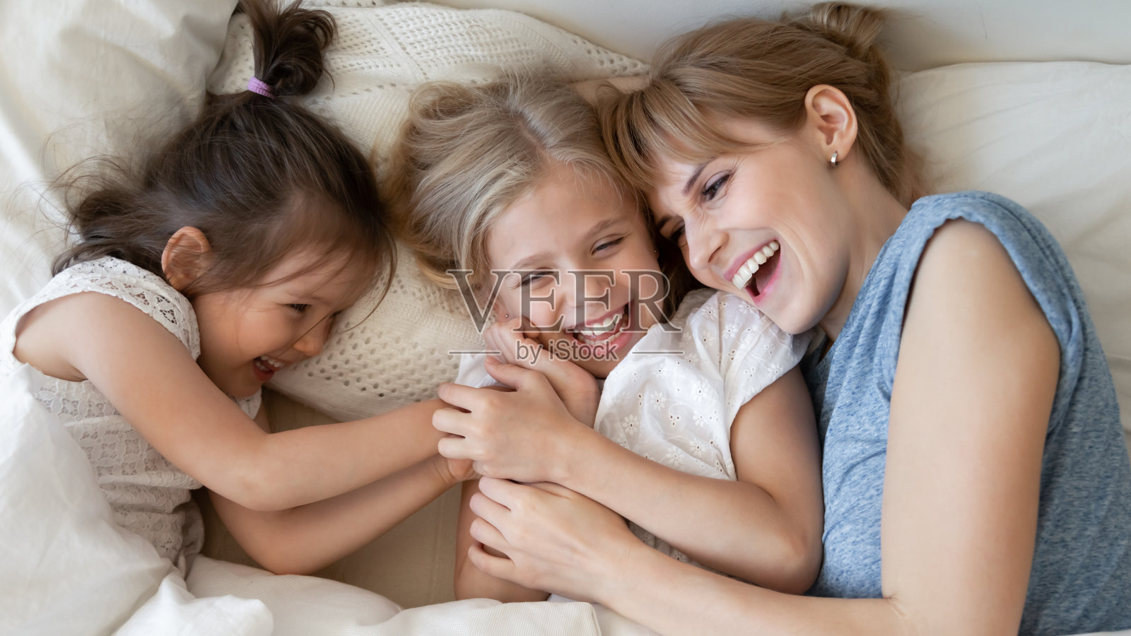 一个快乐的家庭，母亲微笑着和两个女儿躺在一起。照片摄影图片