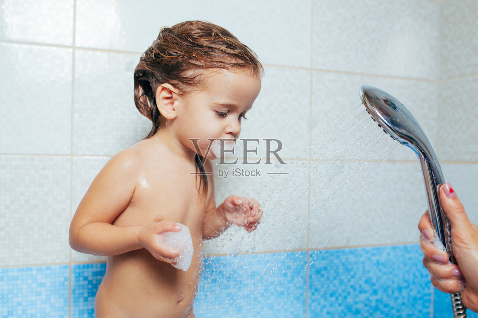 漂亮的小女孩正在洗澡。孩子们玩着水，然后从淋浴器里喷水。快乐的孩子们的卫生。淘气的女儿在浴室里照片摄影图片
