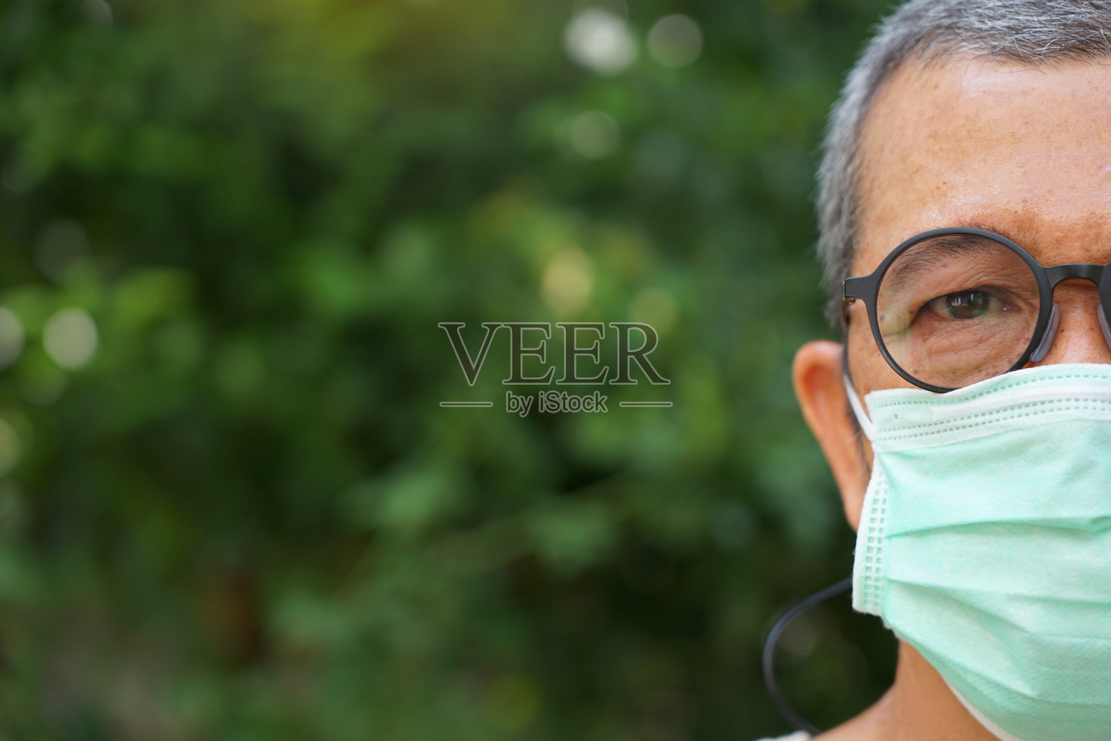 这位老人戴着外科口罩，把脸半掩起来，保护自己免受病毒和流感的侵袭照片摄影图片