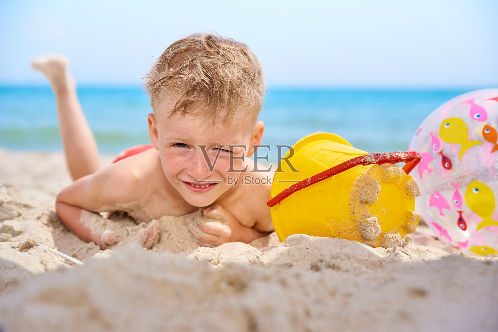 小男孩躺在沙滩上。照片摄影图片