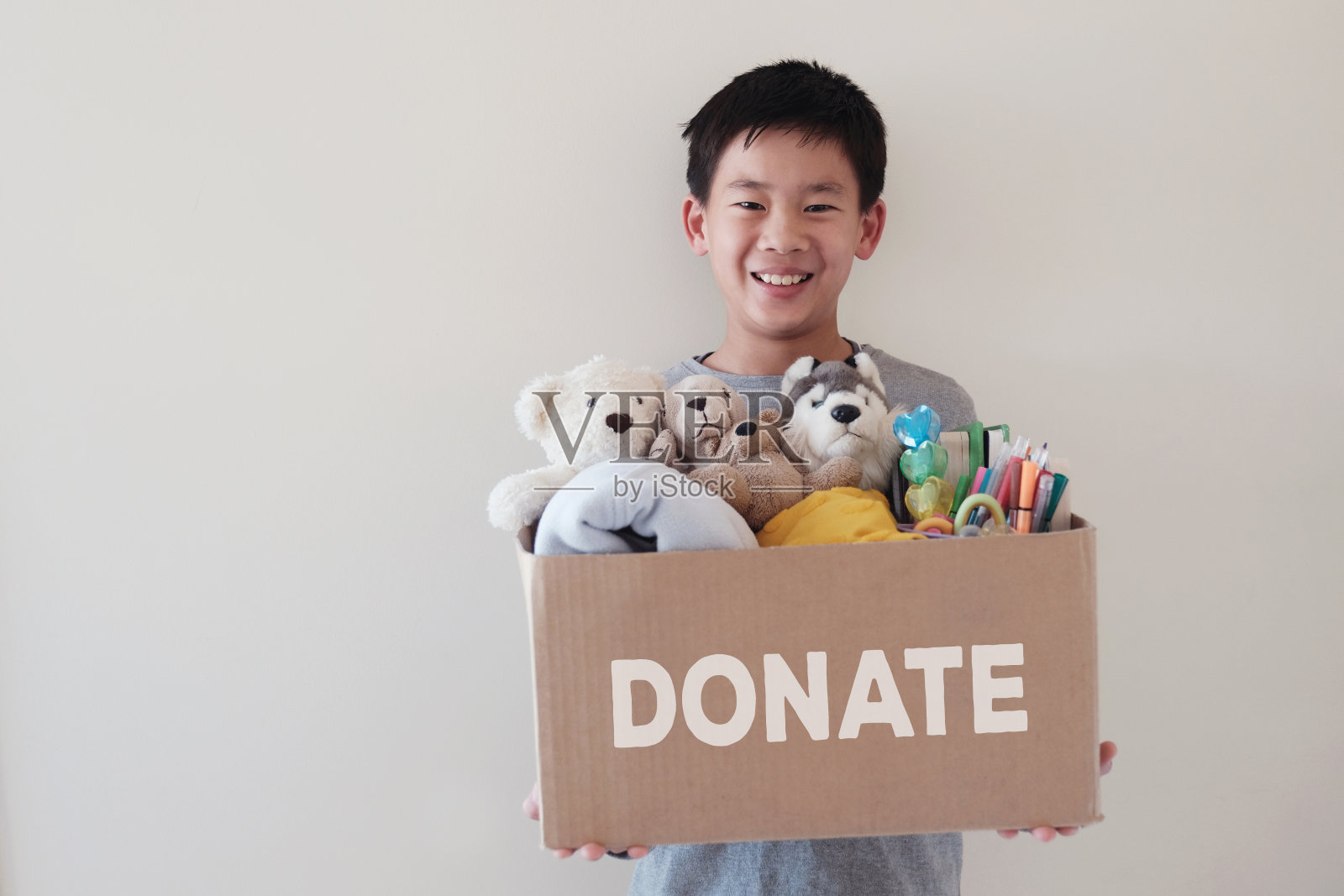 混合亚洲青年志愿者十来岁的男孩拿着一个装满了二手玩具，布料，书籍和文具的盒子捐赠照片摄影图片
