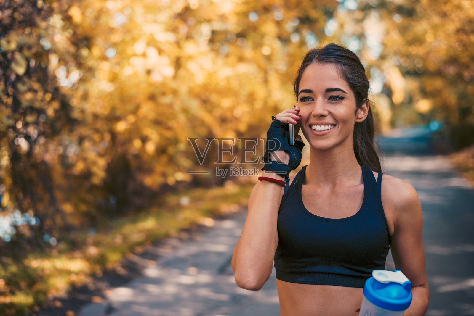 微笑的女孩穿着运动服在秋天的城市公园打电话。照片摄影图片