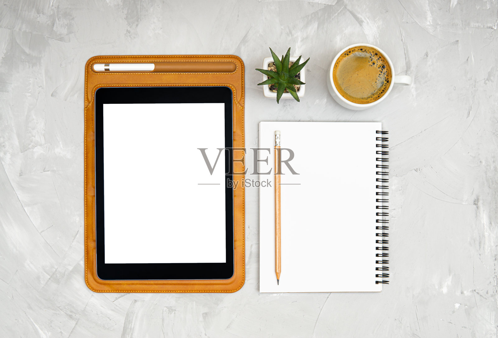 皮套的平板电脑，螺旋笔记本，铅笔，笔，小桌上花和一杯咖啡在一个具体的背景。俯视图，平放。照片摄影图片