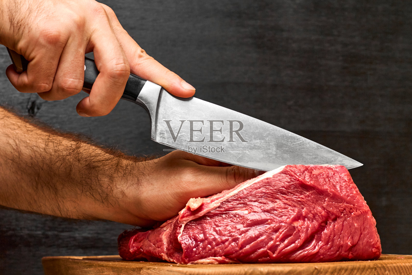 特写男子的手切牛肉与刀在一个黑色的背景。健康蛋白粉的概念。照片摄影图片