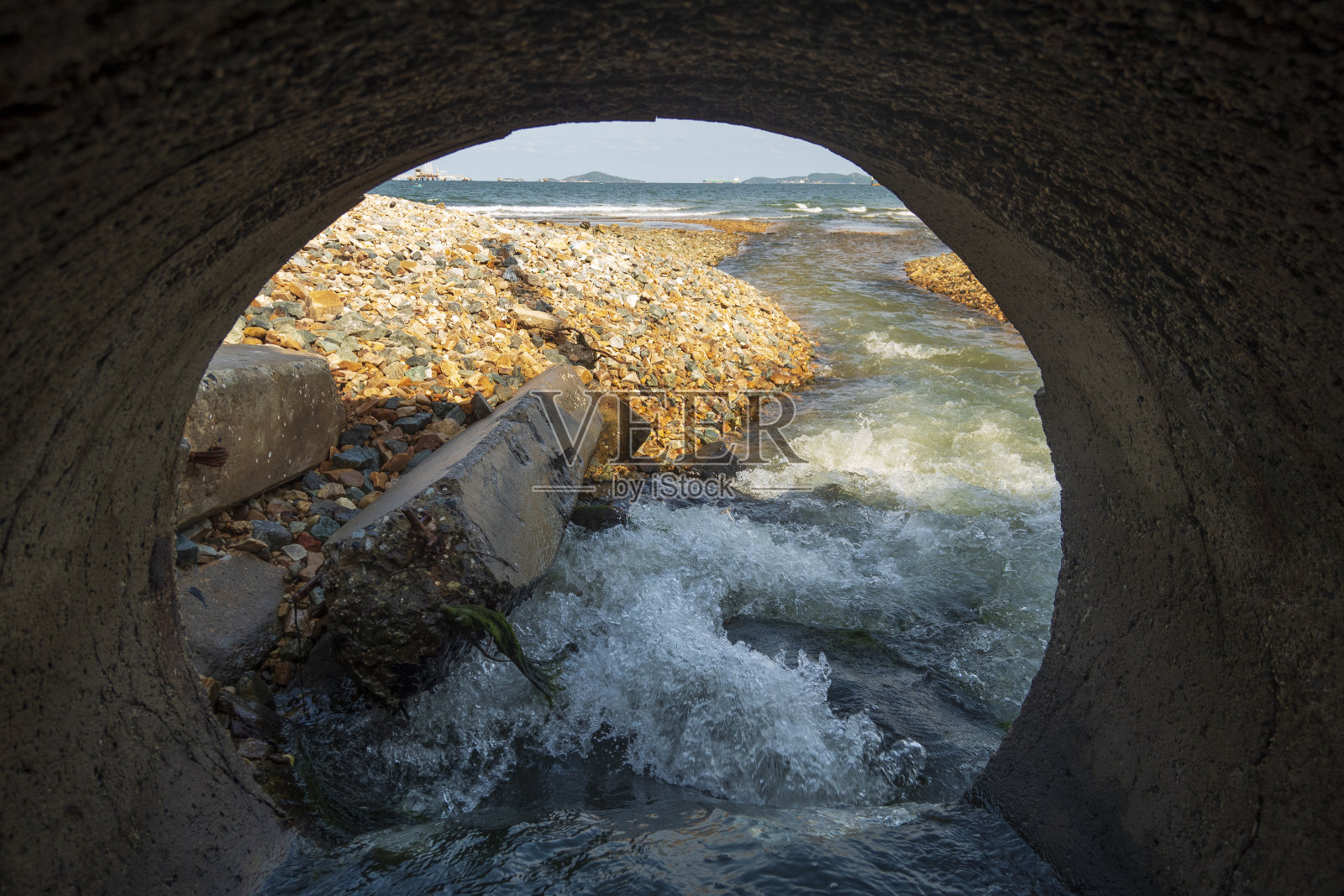 在一个工业工厂排放到海里的下水道隧道的内部视图。工业废水污染肮脏的污水从排水沟流到海边的沙滩上。“n照片摄影图片