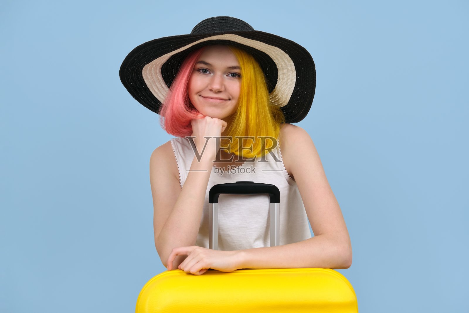 摄影室里的年轻女子戴着夏天的帽子和手提箱。照片摄影图片